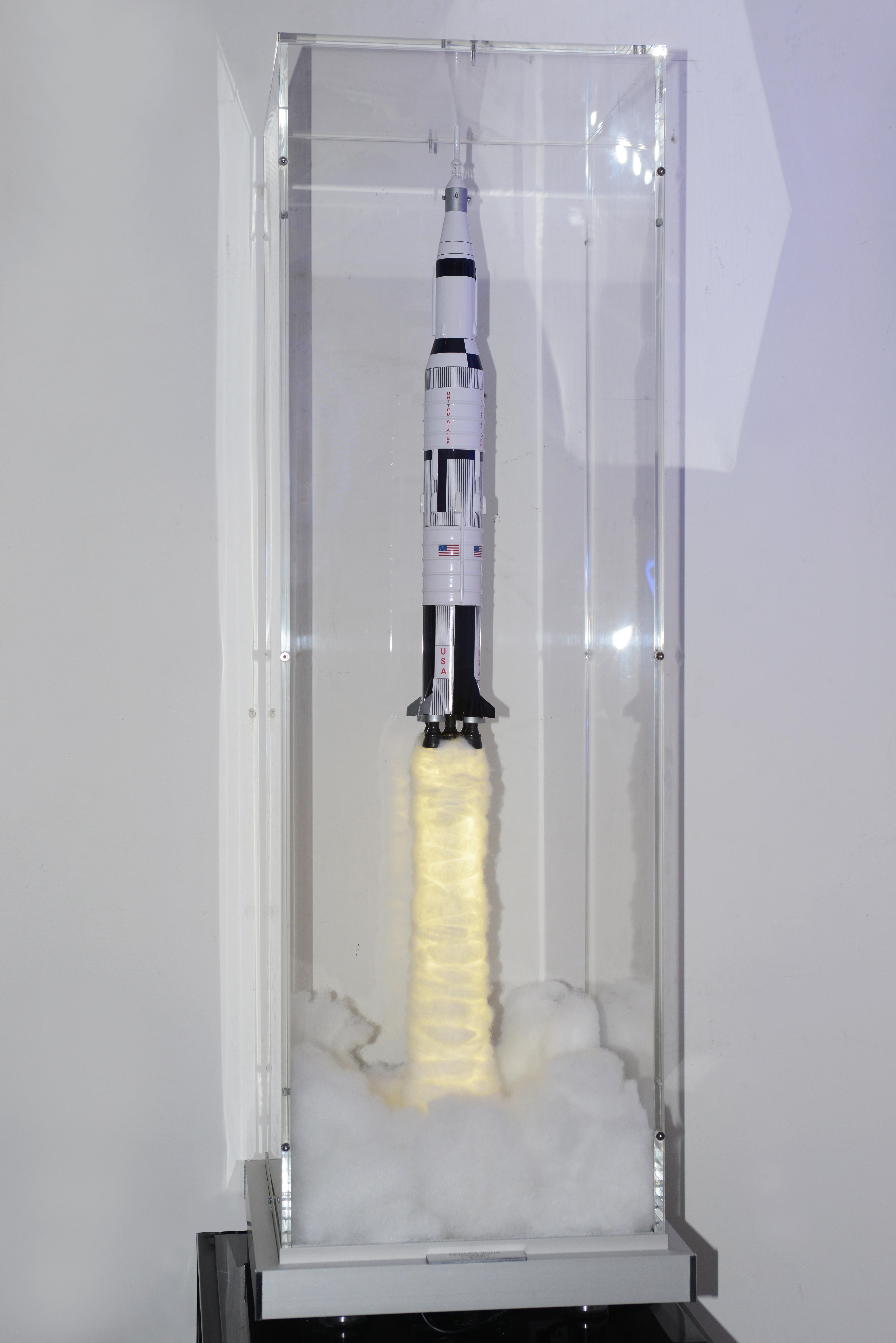 Sculpture Rendez-Vous Fusée Saturn V
avec structure en bois verni.
Pièce peinte à la main. Fusée sous
boîte en plexiglas ultra clair, avec fumées
pour créer l'effet de décollage. Fumée 
est éclairé par un système de diodes électroluminescentes. Avec