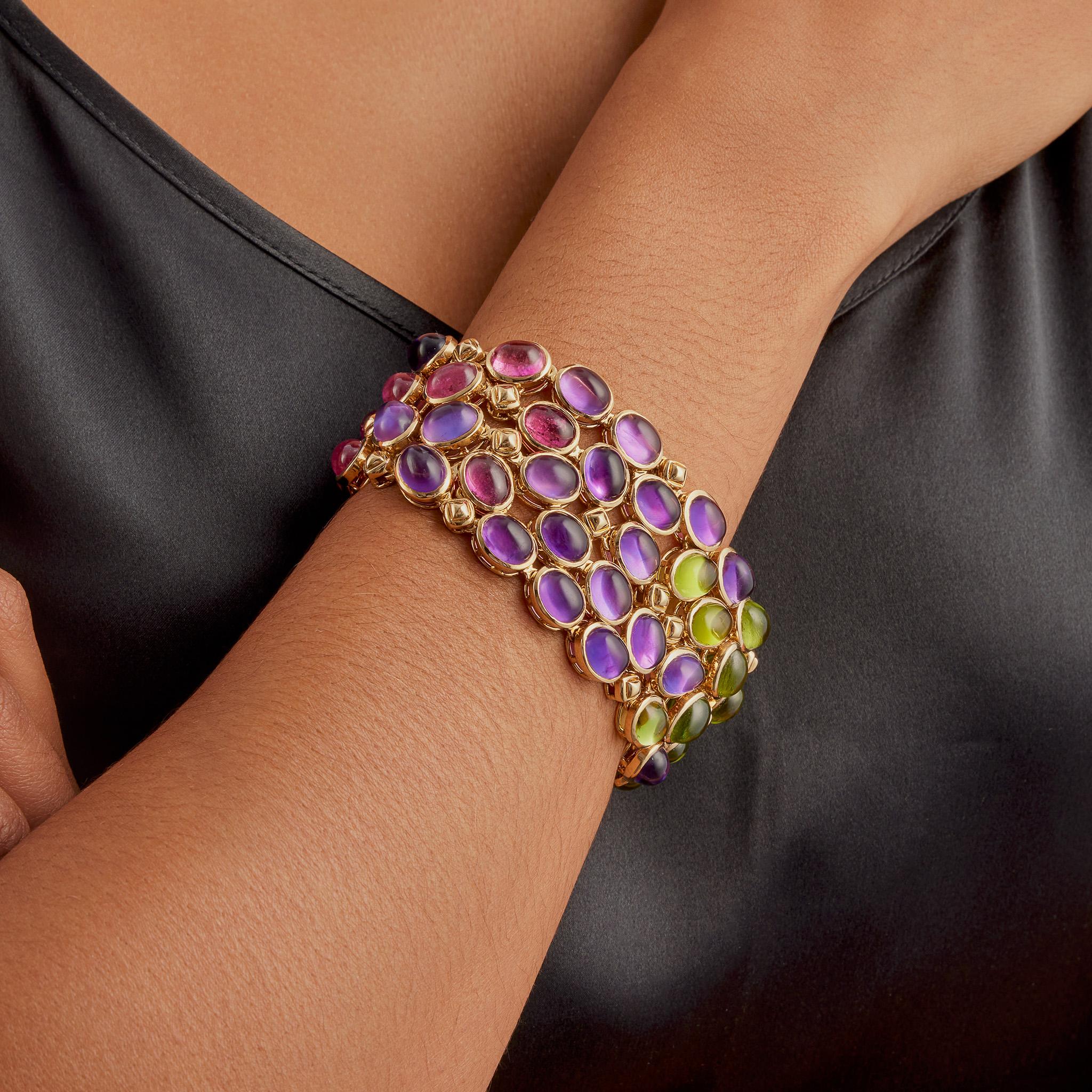 Dating from the 1980s, this strap bracelet by Maison René Boivin is composed of sapphire, pink tourmaline, perdiot,and amethyst, set in 18K gold. The fully flexibly tapering strap is composed of a mesh of oval cabochons subtly graduating in hue from