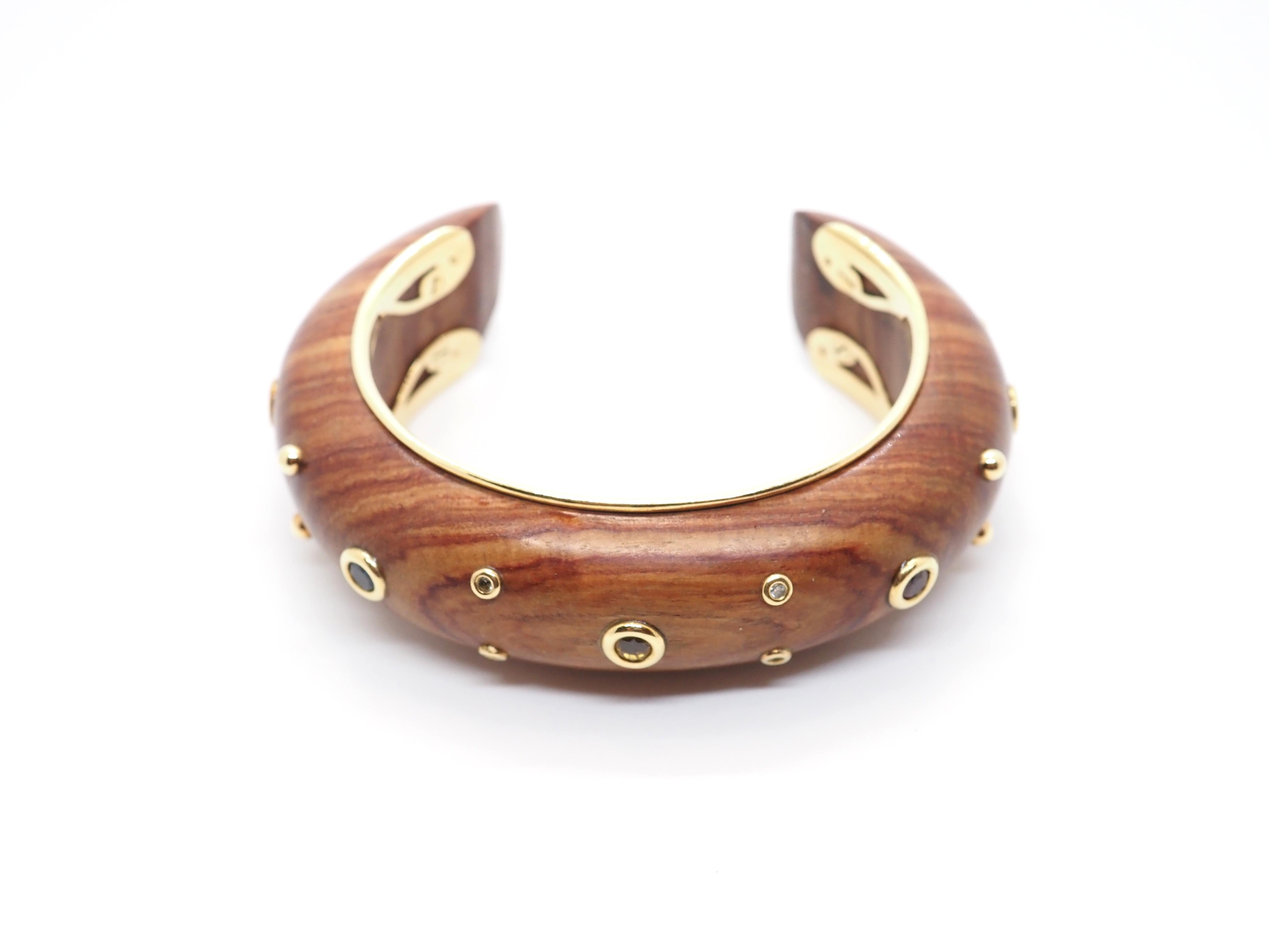 Original set of earrings, ring and bracelet  signed by Rene Boivin, made in wood, yellow gold and different gem stones.  
Cuff bracelet in wood surrounded by 2 lines of gold,  decorated with two round cut emeralds, of 2.70mm each, one round cut 