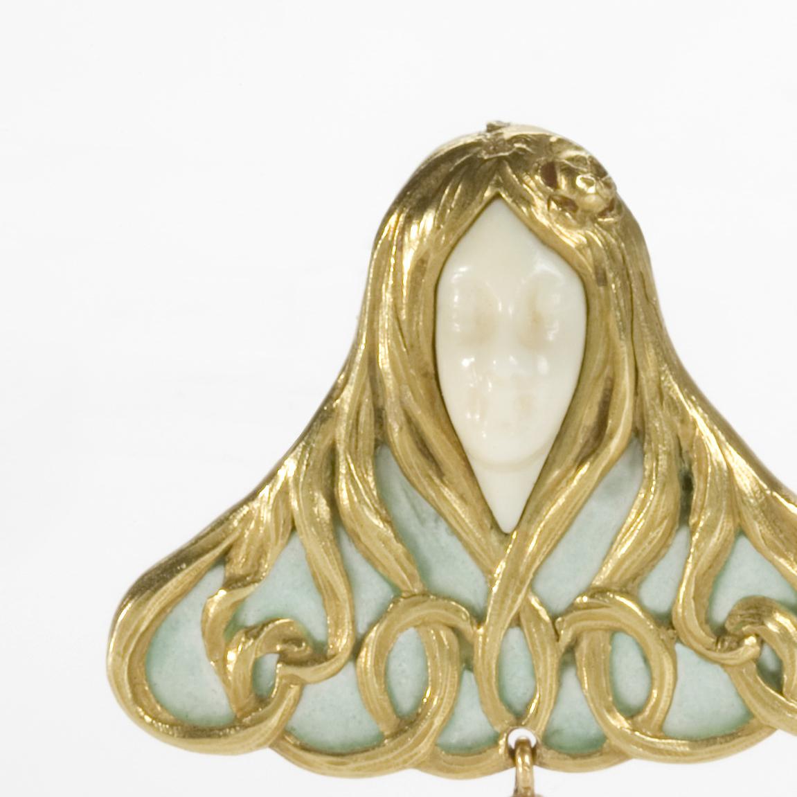 This Art Nouveau brooch, composed of gold, carved white coral, freshwater pearl, and plique-à-jour enamel, dates from 1900, and is the work of the Parisian jeweler, René Foy. The figural form depicts a woman, whose face is carved in white coral,
