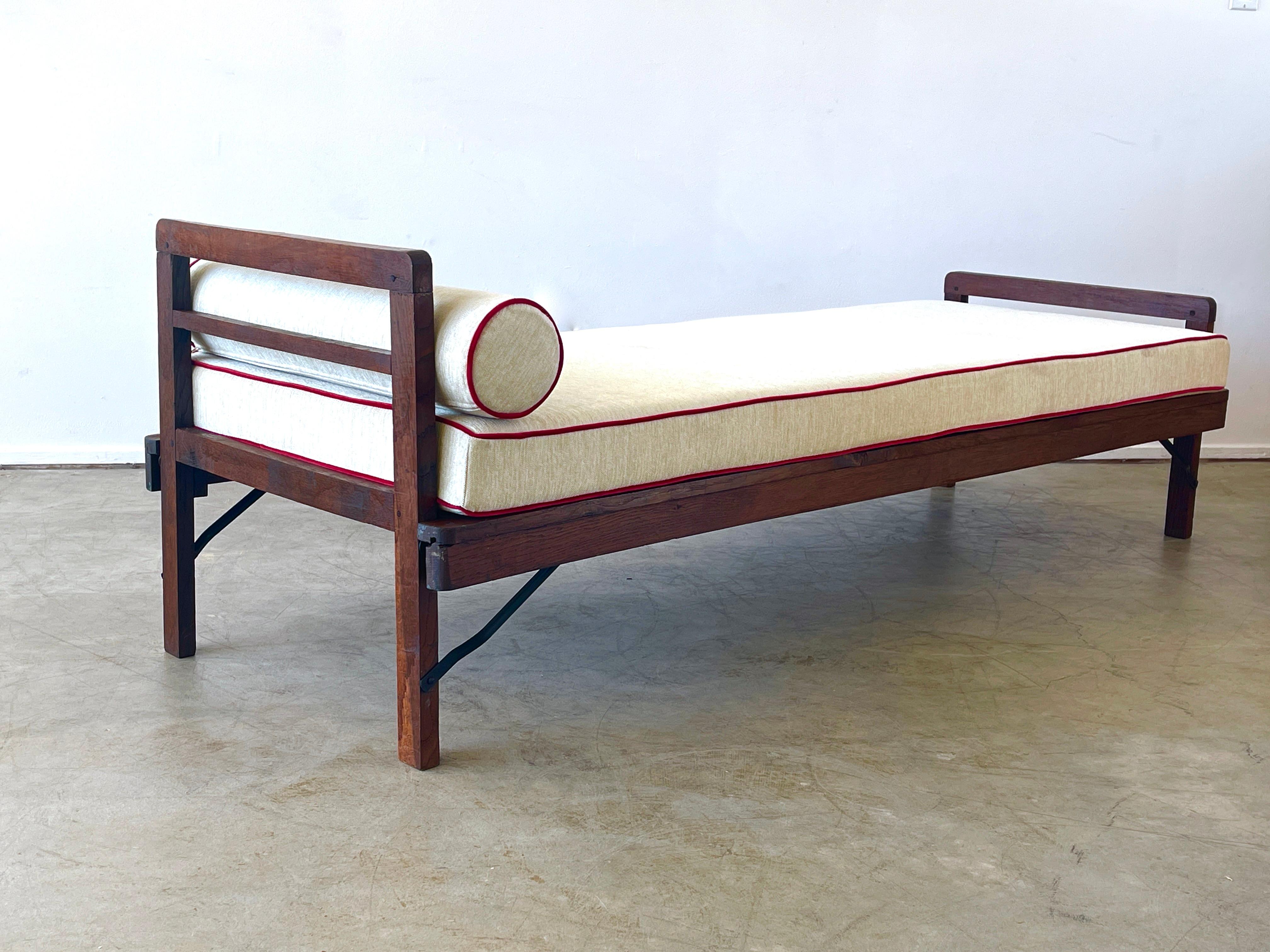 Rene Gabriel daybed with oak headrest and footrest.
Collapsible legs fold inward with wonderful patina.
Original seat cushion and bolster upholstered in France in cream chenille and red piping.