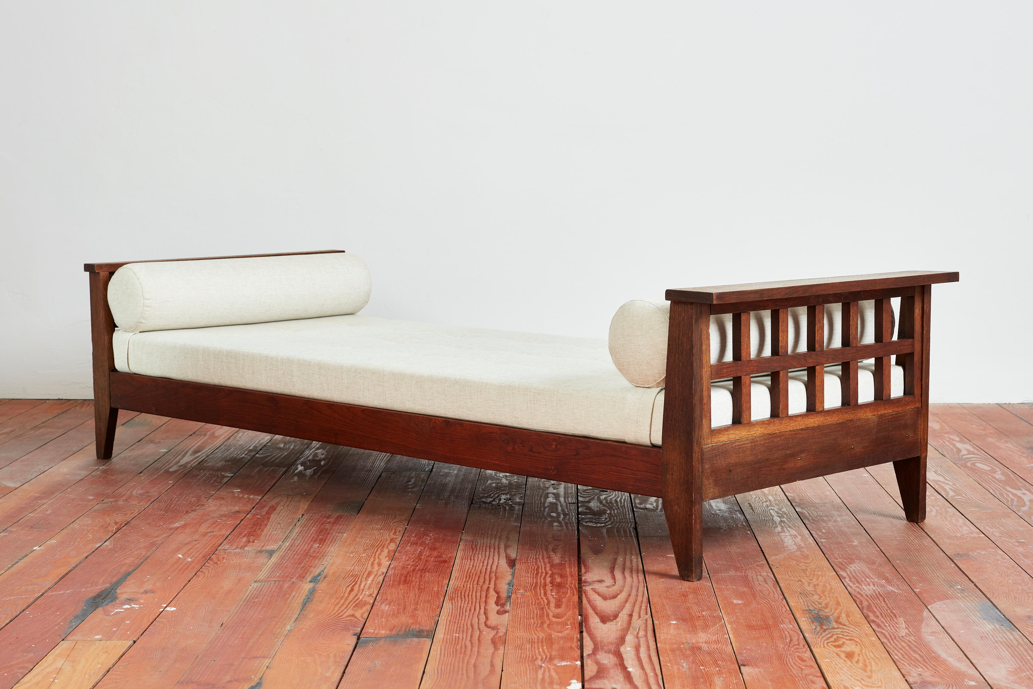 Rene Gabriel daybed - France, circa 1940s
Beautiful oak patina with cross brass frames on headboard and footboard 
Newly reupholstered in France in beige linen 
Bolster cushion on both ends
Angular legs.