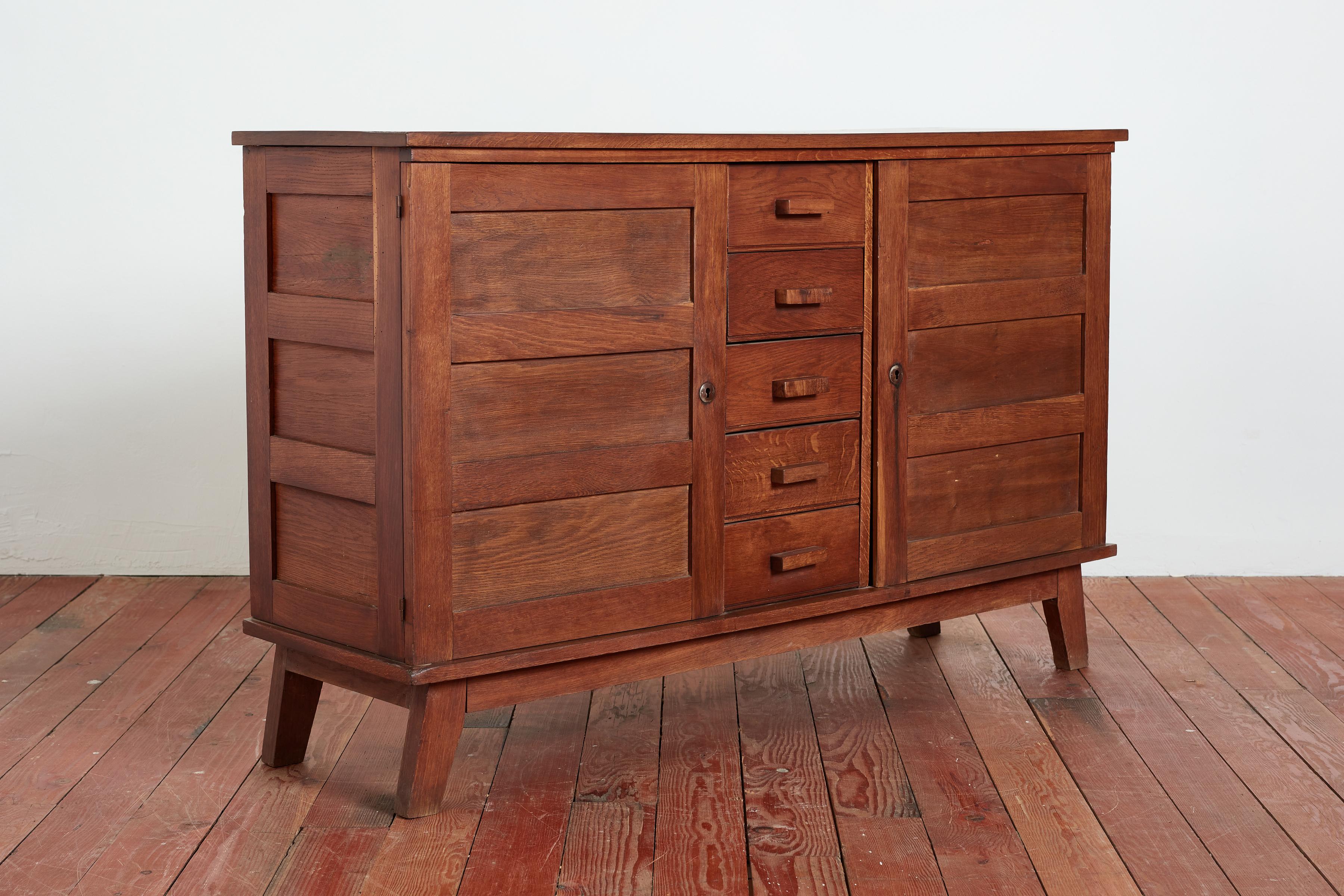 Gorgeous sideboard by Rene Gabriel with great angled lines and wood patina Cabinet has 2 swinging doors with 5 center drawers and thick wood handles. Original locking hardware. 
