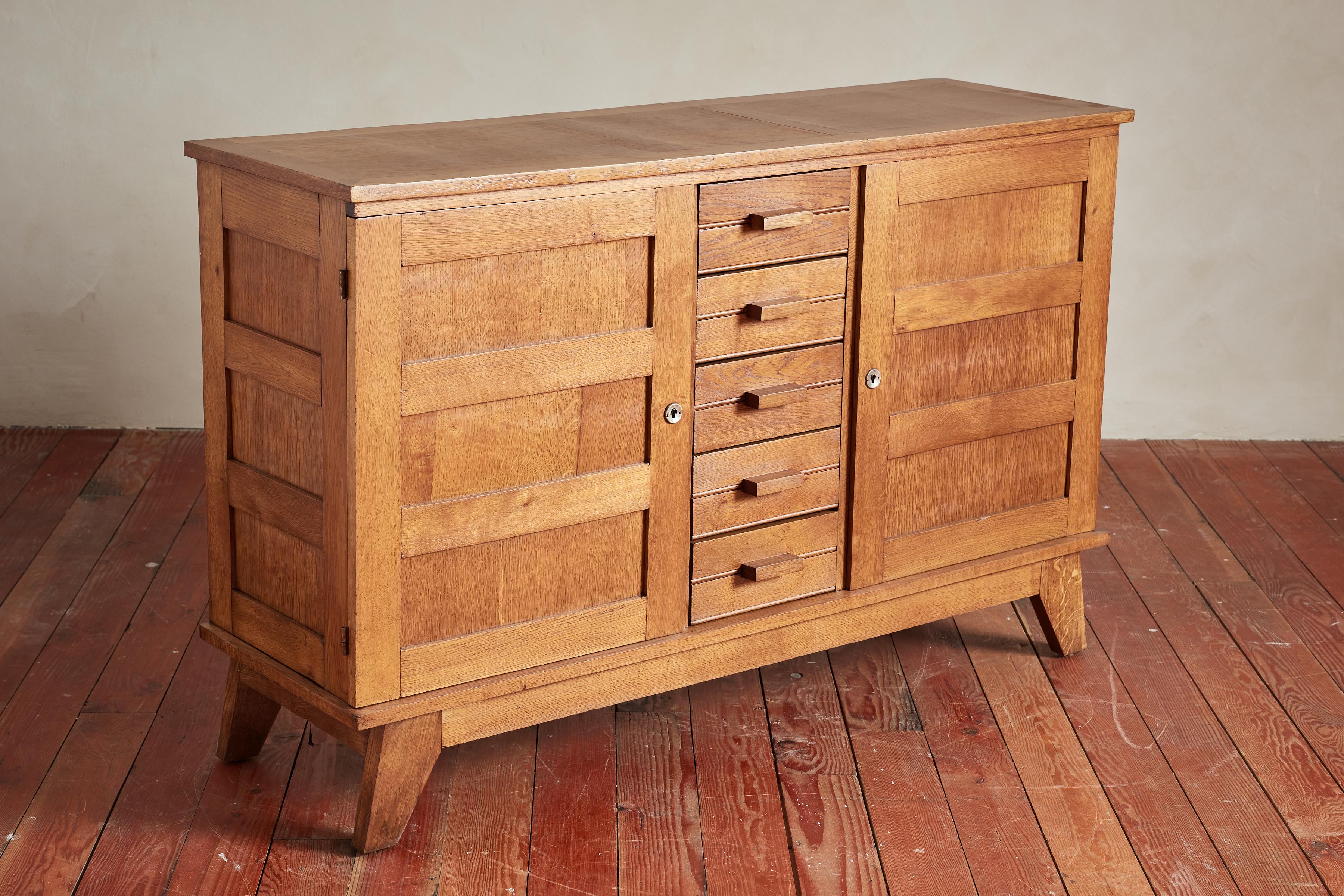 Wonderful sideboard by Rene Gabriel with great angled lines and wood patina.

Cabinet has 2 swinging doors with 5 center drawers and thick wood handles. 

Original locking hardware.

France, 1940s