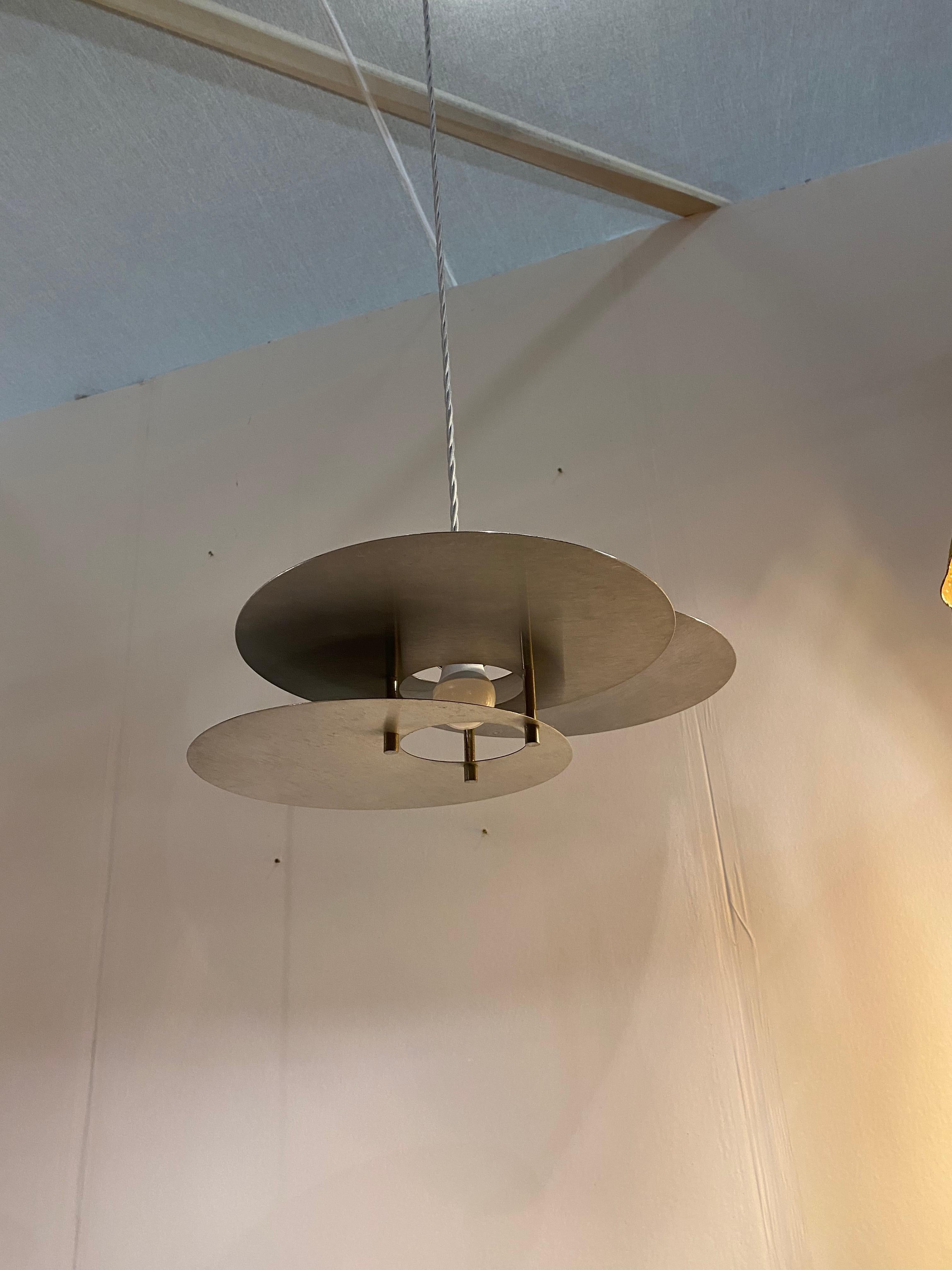 A rare example of sculptural Mid-Century Modernist Bauhaus pendant light consists of three circular polished aluminium geometric discs configured in a stacked over-lapping fashion with a central hole on all discs where the lamp holder is. All three
