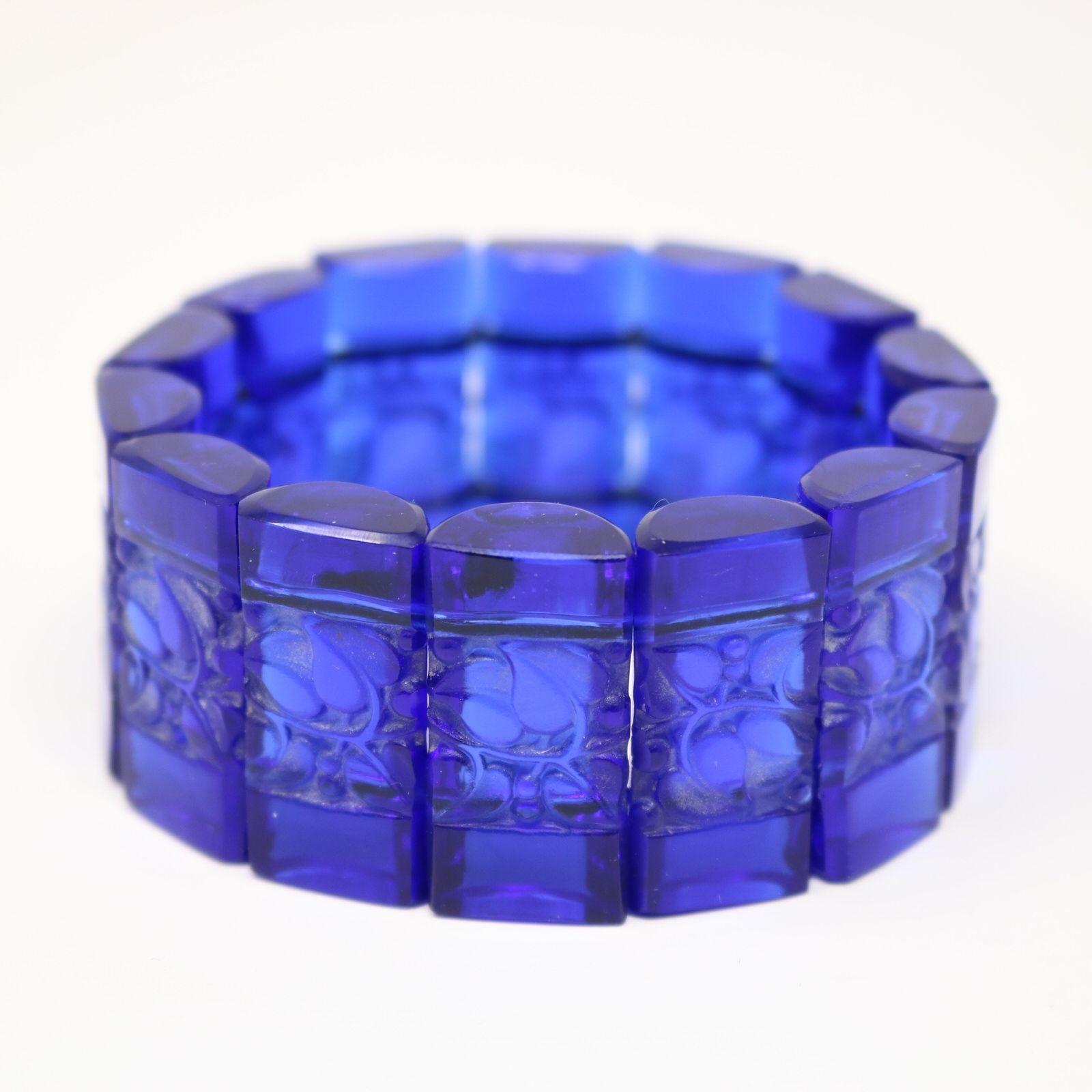 Bracelet 'Ceriser' de René Lalique en verre bleu. Le bracelet se compose de 14 pastilles rectangulaires, en forme de demi-cylindre, reliées entre elles par un élastique. Chaque tablette est décorée de feuilles et de baies moulées. Marque de fabrique