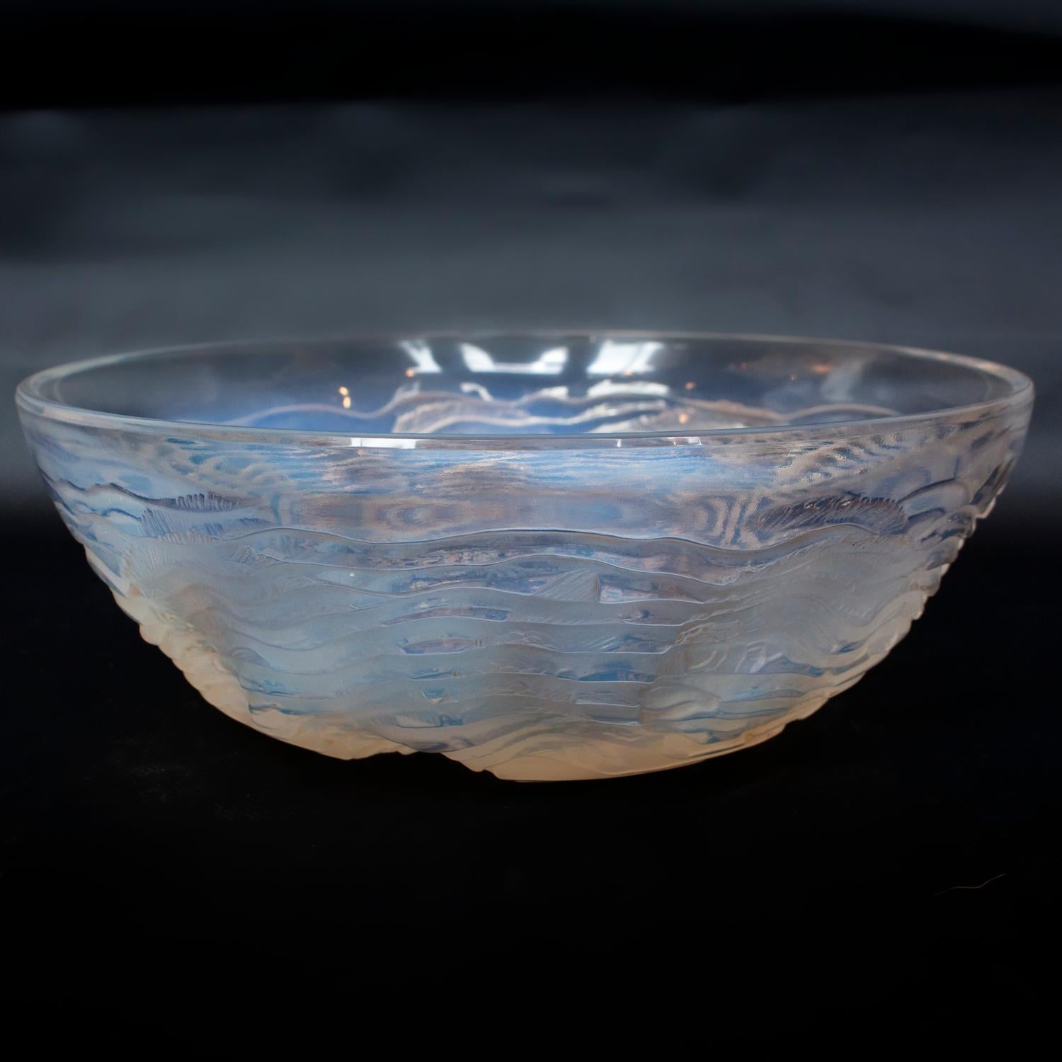 Dauphins, an Art Deco glass bowl. Opalescent and clear glass, decorated over with reverse raised motifs of stylized dolphins swimming through ripples of water. 

Signed R. Lalique to underside.

Literature: Marcilhac Catalogue Raisonné de