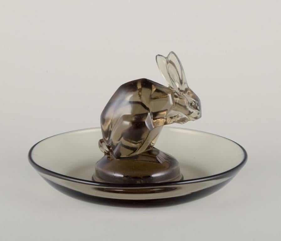 René Lalique, France. 
Early Art Deco pin dish with a rabbit in smoked art glass.
Approximately from 1930.
Model number 285.
Signed.
In perfect condition.
Dimensions: H 6.0 cm x D 9.3 cm.