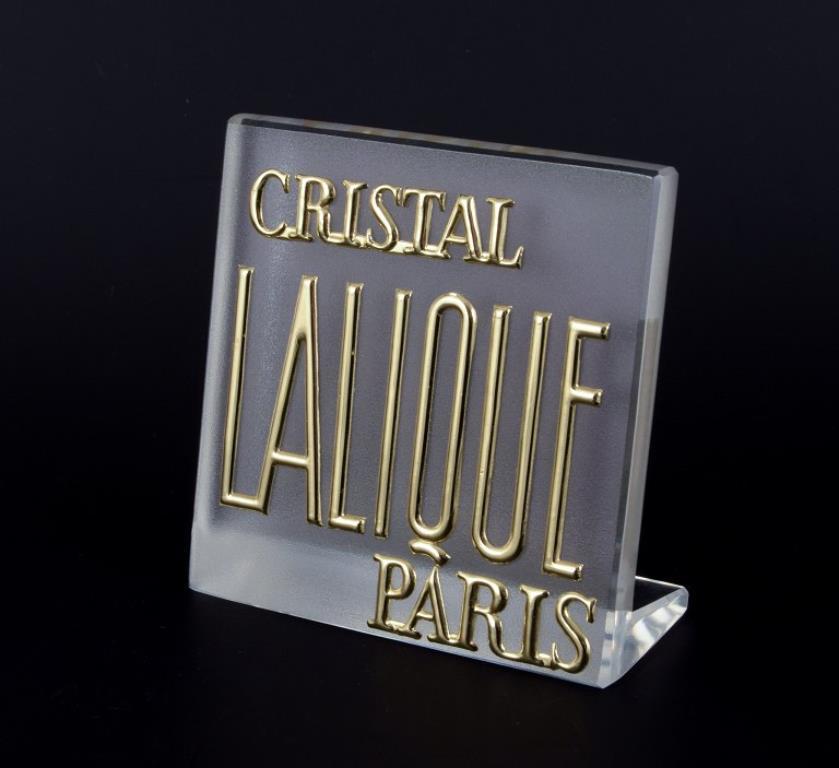 René Lalique (1860-1945), Francia. 
Cartello espositivo/insegna del negozio in vetro parzialmente satinato. Scritte in oro. 
1970/80s. 
Condizioni perfette. 
Dimensioni: L 9,5 cm x H 9,5 cm x P 4,5 cm.