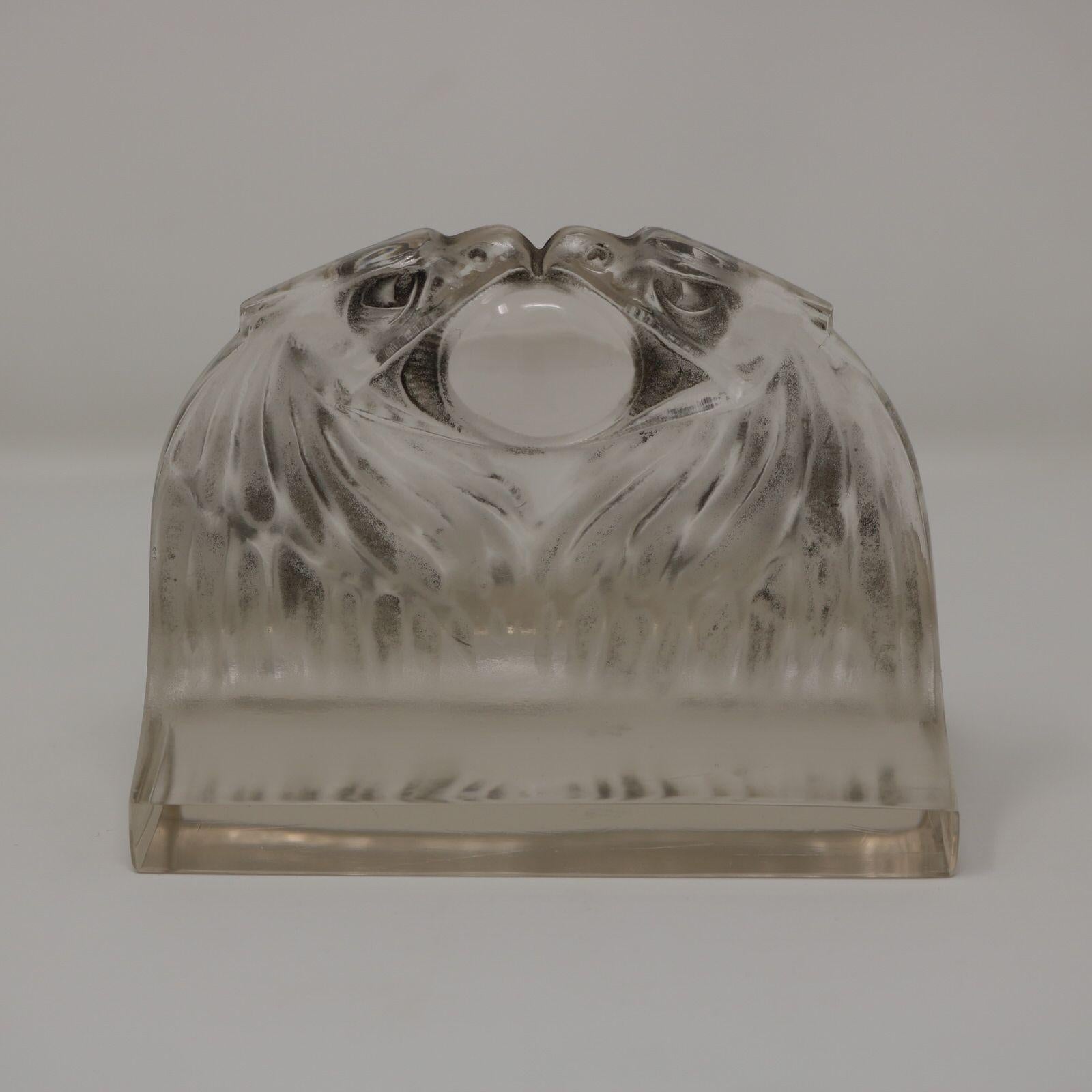 Briefbeschwerer 'Deux Aigles' von Rene Lalique aus klarem und mattiertem Glas, mit grau gebeizten Details. Zwei Adlerköpfe stehen sich gegenüber und haben einen Ball im Schnabel. Geformte Herstellermarke 