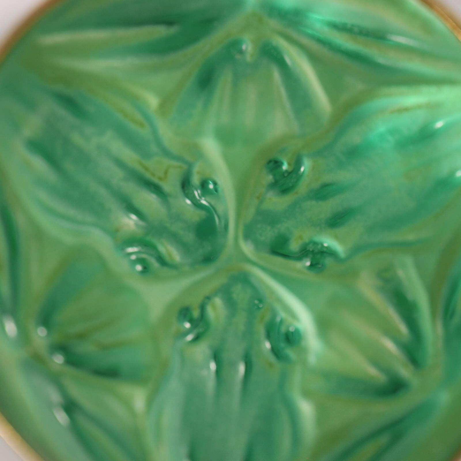 Spilla Grenouilles in vetro di Rene Lalique. Vetro trasparente con macchie verdi, con supporto in pellicola. Questo schema presenta un Trio di rane. Incastonato in una montatura color oro con spilla. Marchio del produttore 