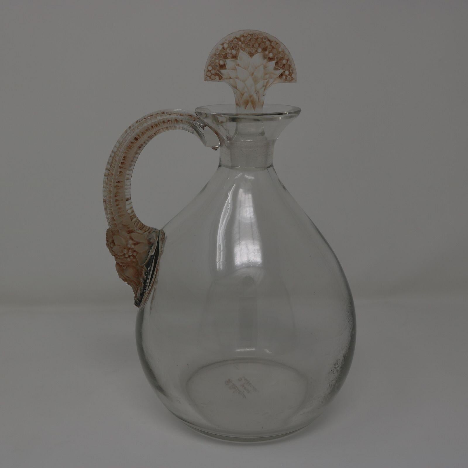 Rene Lalique clear glass 'Satyre' decanter, with brown patina details. Has a bulbous shaped bottle, with a handle on one side. The base of the handle is in the form of a satyr head with long horns curving up to form the handle. The glass stopper has