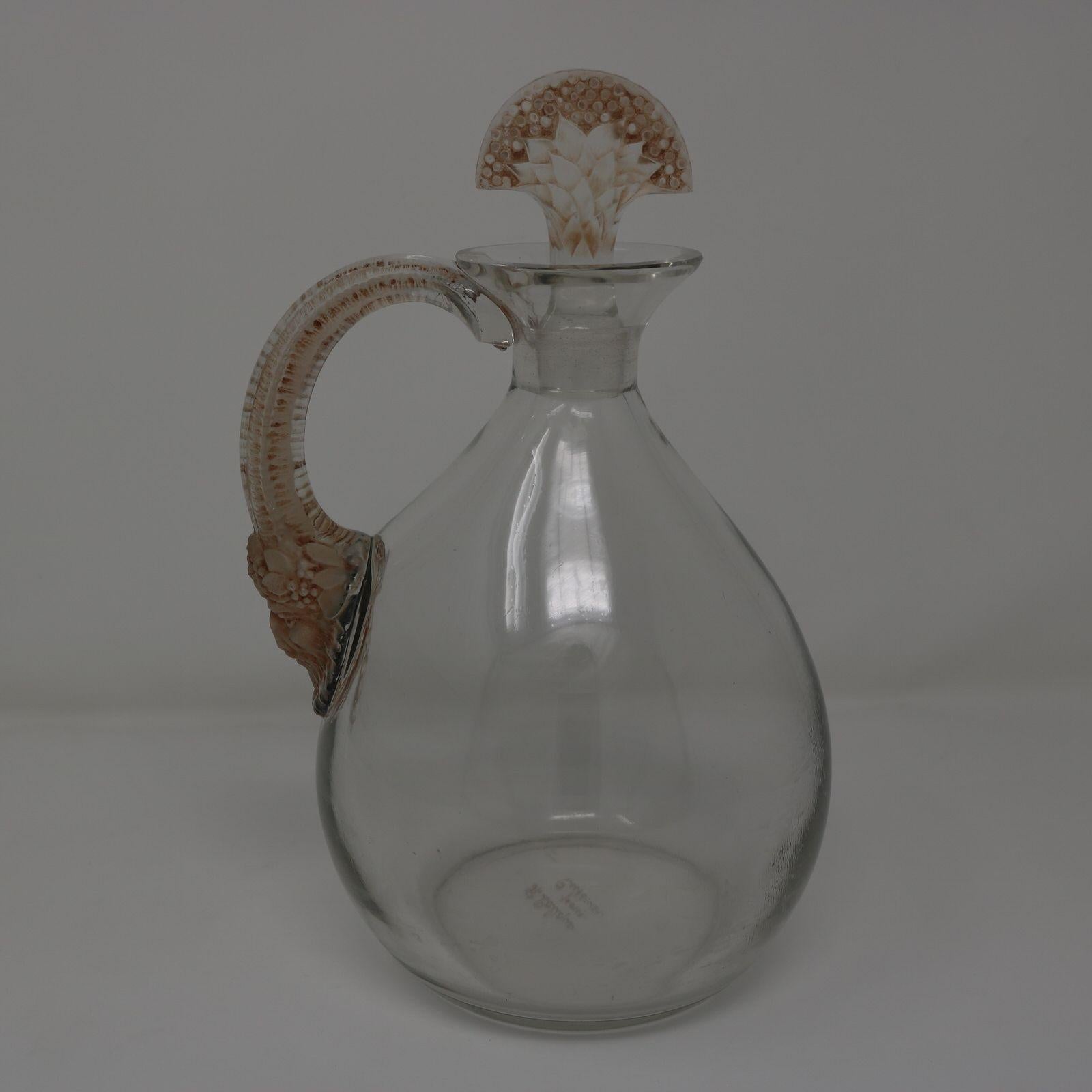 Dekanter 'Satyre' von Rene Lalique aus Klarglas, mit brauner Patina. Hat eine bauchige Flasche mit einem Griff an einer Seite. Die Basis des Griffs hat die Form eines Satyrkopfes mit langen Hörnern, die sich zum Griff hin aufbiegen. Der Glasstopfen