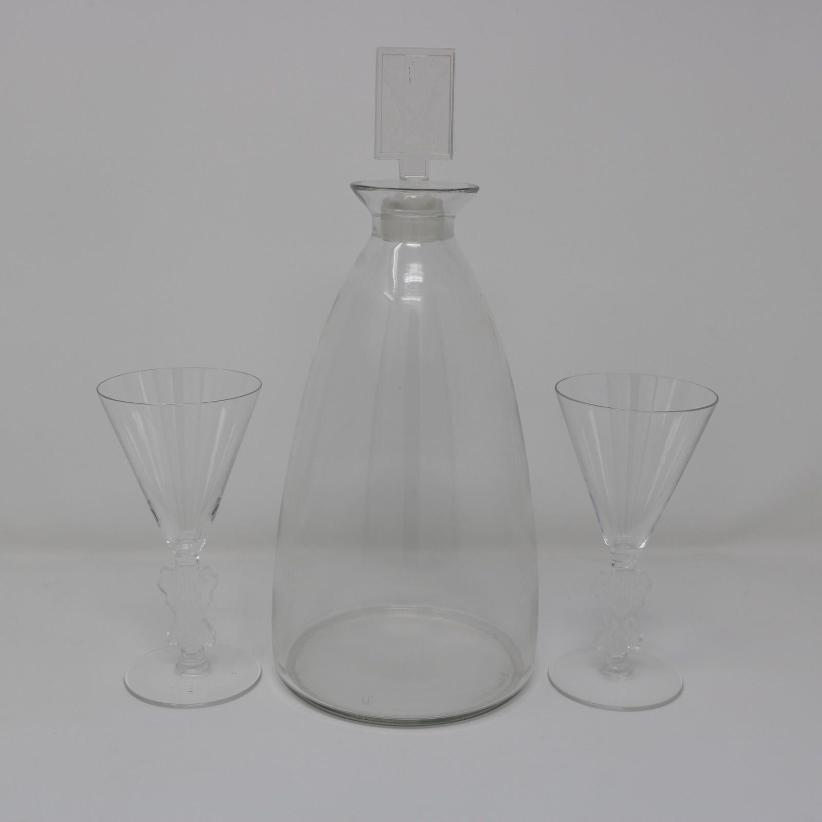 Rene Lalique Glass 'Strasbourg' Decanter with two matching glasses. The rectangular shaped stopper features two men grape stomping. The stems of the glasses feature the same motif. Makers mark, 'R Lalique France' and pattern number, 'No.5082'