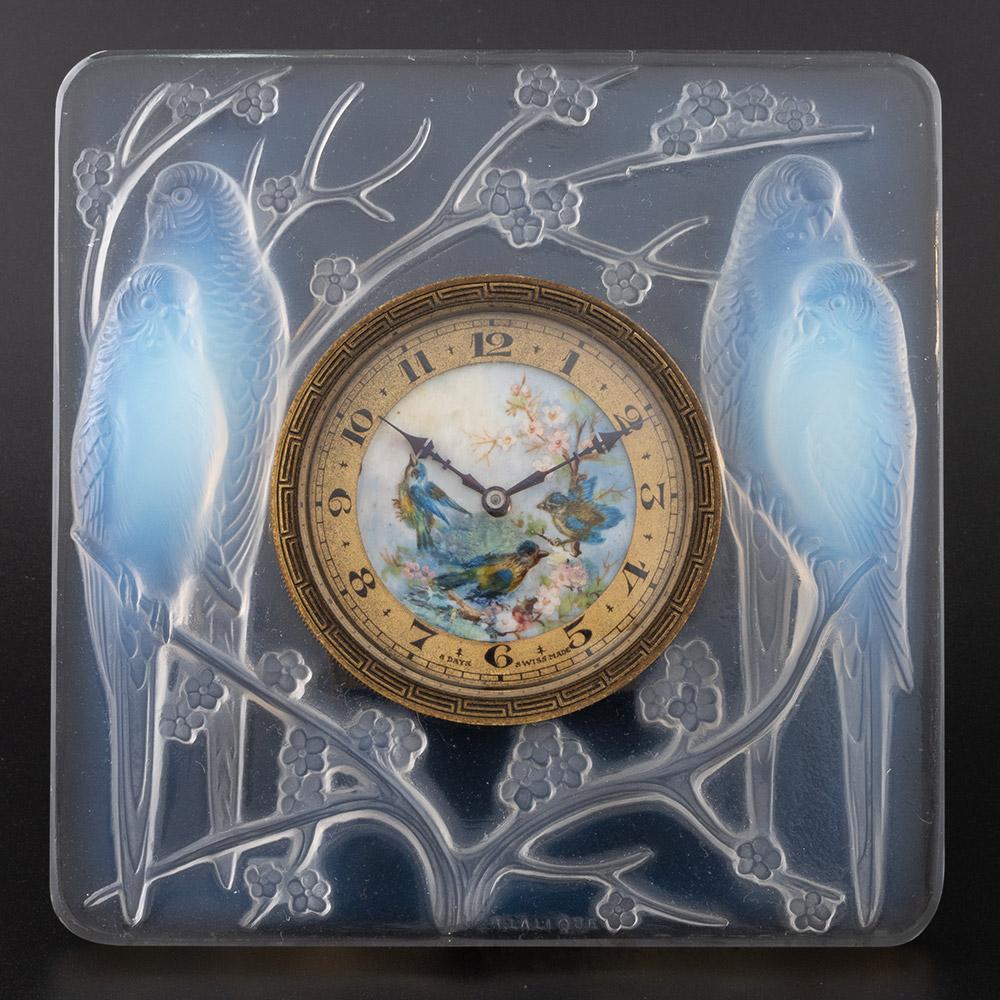 Typ: Rene Lalique Inseperables Uhr - Marcilhac 765
Datum : Entworfen 1927
Herkunft: Wingen-sur-Moder, Frankreich
Beschreibung : Die Einfassung besteht aus klarem Glas mit opalisierenden Perücken, die auf blütenbesetzten Ästen sitzen. Die Emaille auf