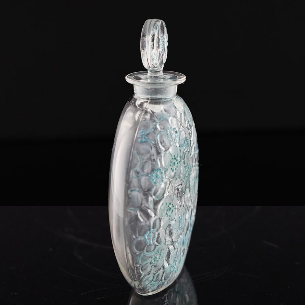 Heading :  Rene Lalique Le Lys perfume bottle
Date : Designed 1920
Origin : Wingen-sur-Moder, France
Colour : Clear with verdigris stain
Stopper : Disc stopper with moulded eglantine petals with Le Lys D'orsay around the stamen
Body : Moulded