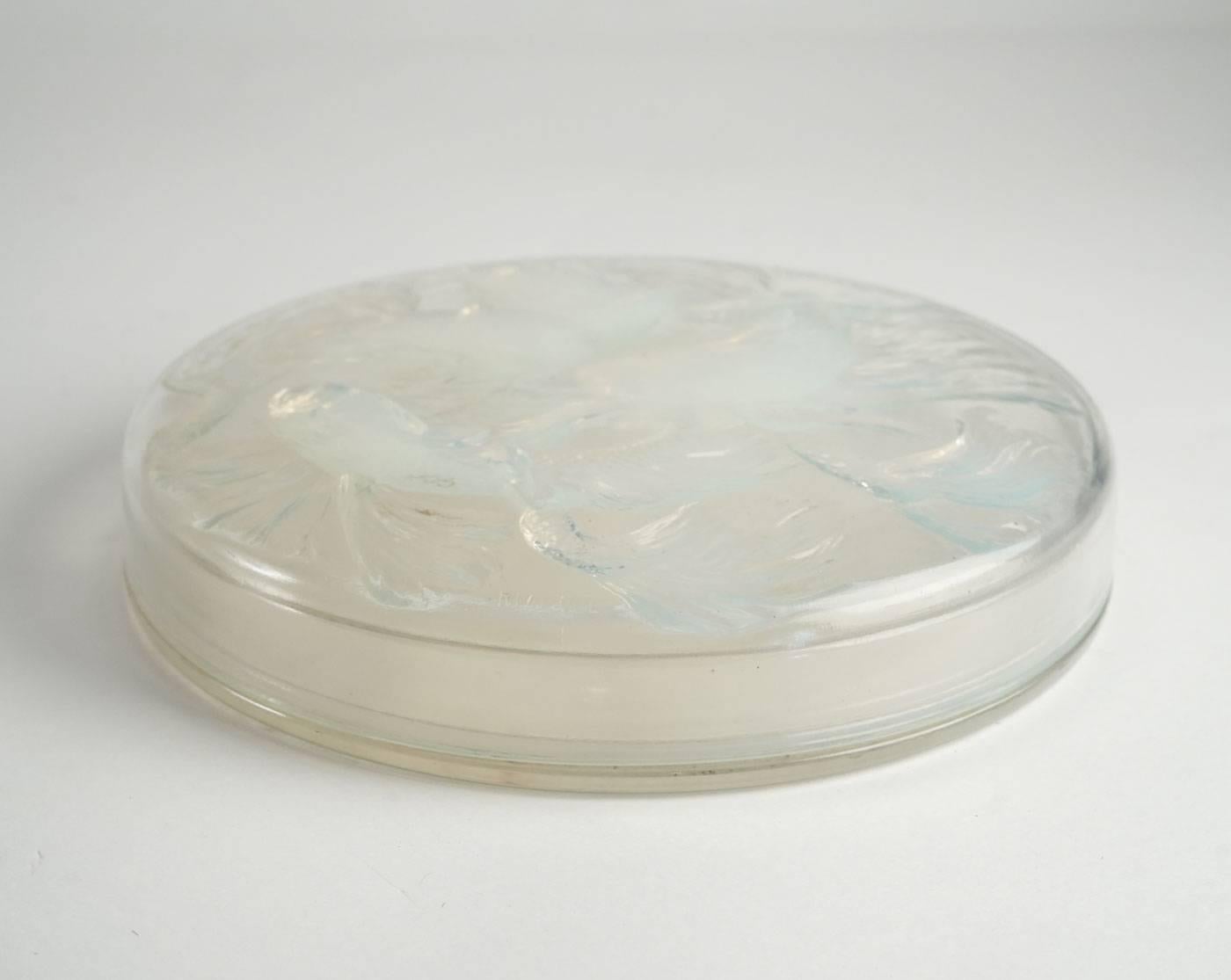 Molded opalescent pressed glass: round opalescent glass fish decorated lid over an undecorated bottom Model: 42, circa 1921.
Two parts glass having a fish motif cover.
Bibliographie:
Félix Marcilhac, “René Lalique, 1860-1945, maître verrier”, les