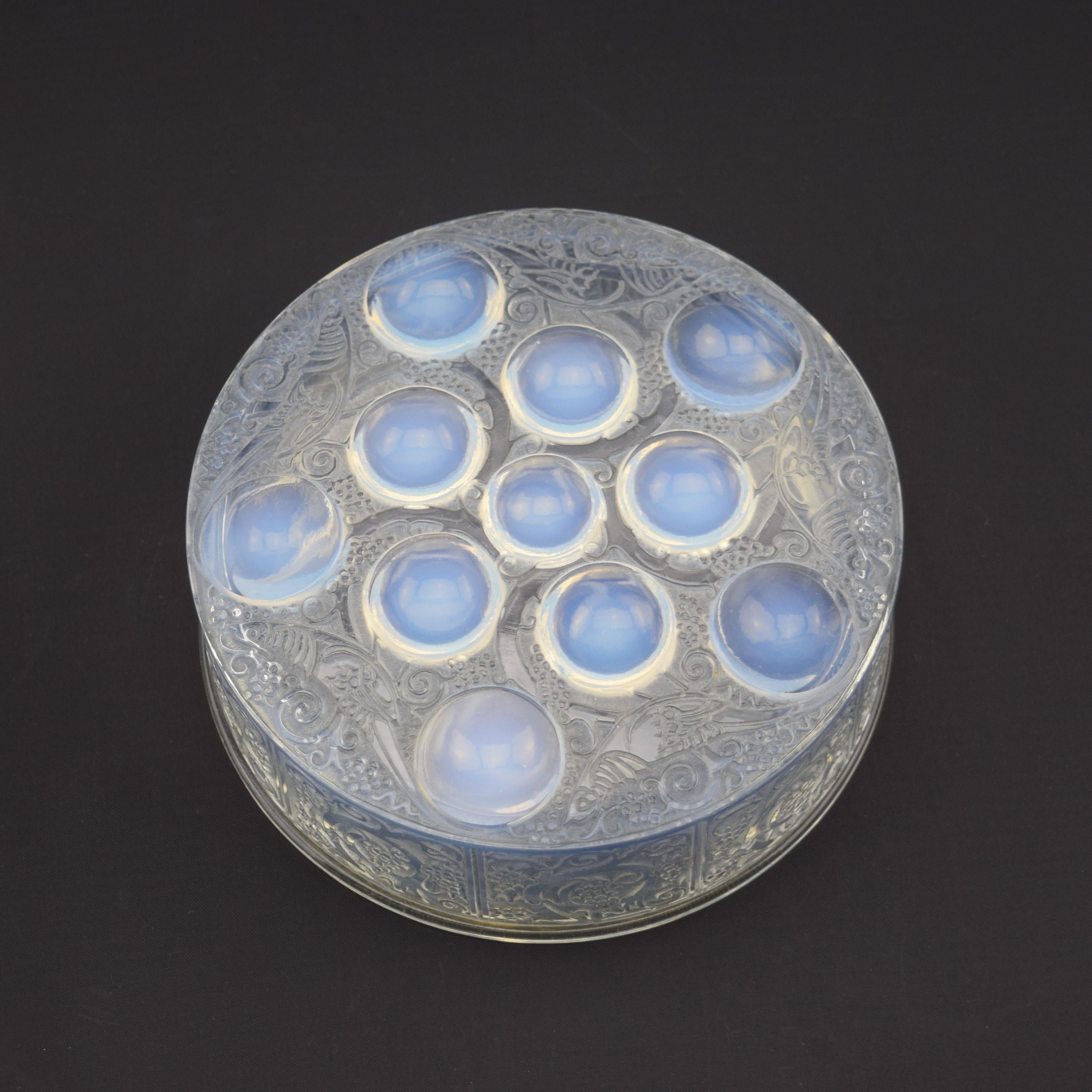Caja Roger opalescente de René Lalique con manchas azul claro. Moldeado con un diseño de pájaros estilizados, follaje y redondeles opalescentes en la tapa.
Marca moldeada Lalique en el lateral de la tapa. El estado es muy bueno, sin daños.

Página