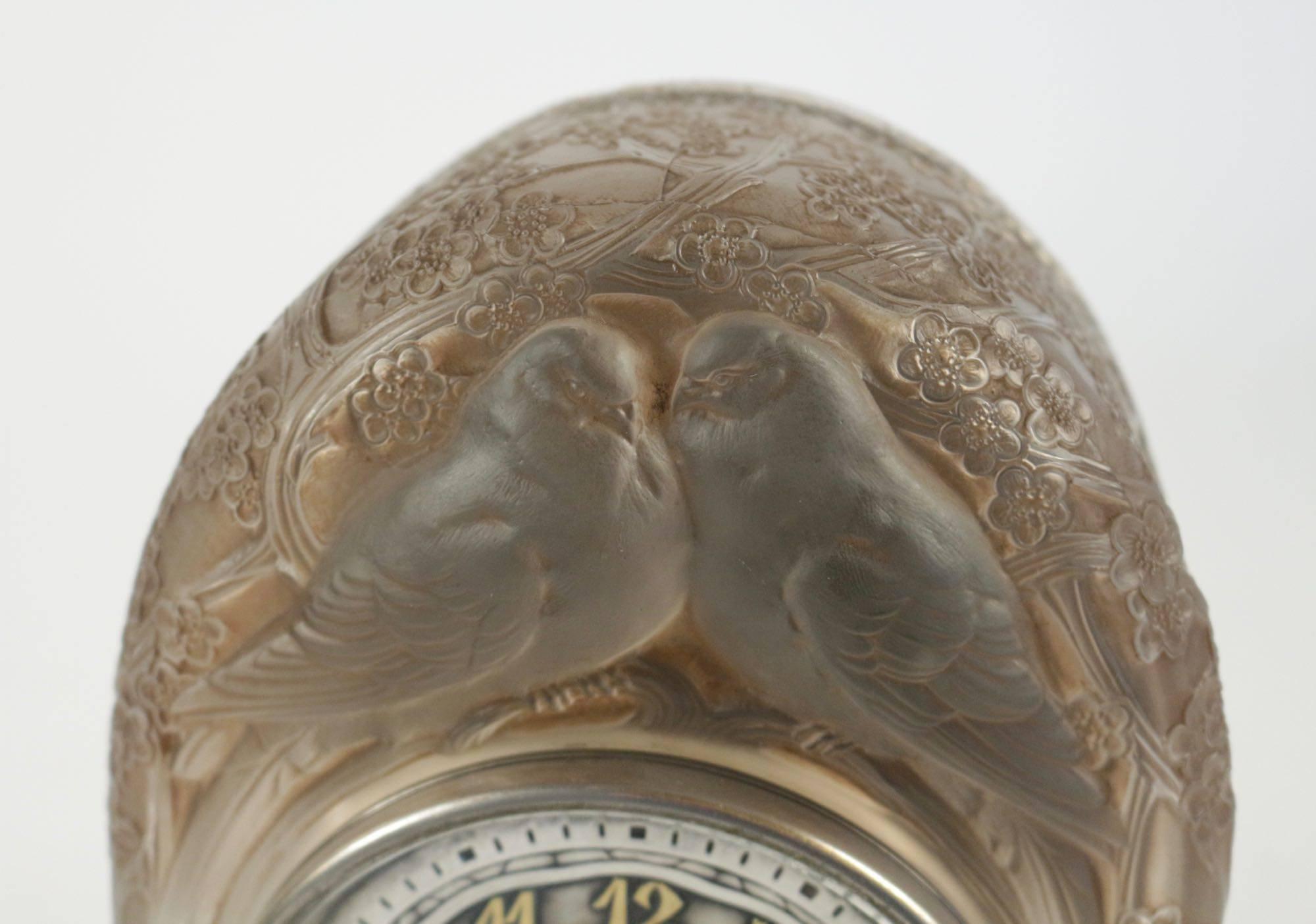 Deux colombes, a moulded-pressed satiny glass mile-stone clock with a Maison ATO milestone dial.
Highlighted with sienna stain.
 Two perched birds on branches and foliage motif under a dome shaped.
Signed R.Lalique, France.
Model created in