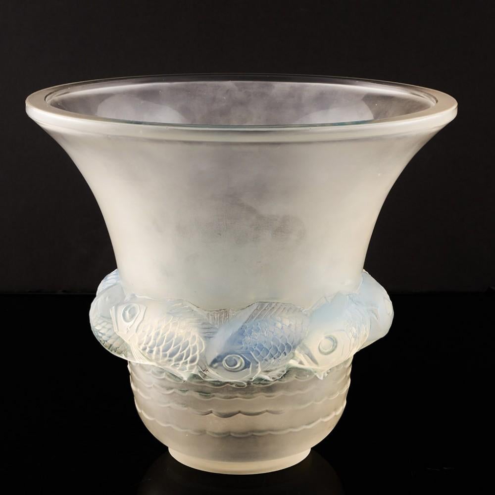 Überschrift: Rene Lalique Piriac Vase
Datum : Entworfen 1930
Herkunft: Wingen-sur-Moder, Frankreich
Merkmale der Schale : Klares und mattiertes Glas mit geformtem, opalisierendem Fischband über einem geformten Wellenmuster.
Markierungen :Geätzte