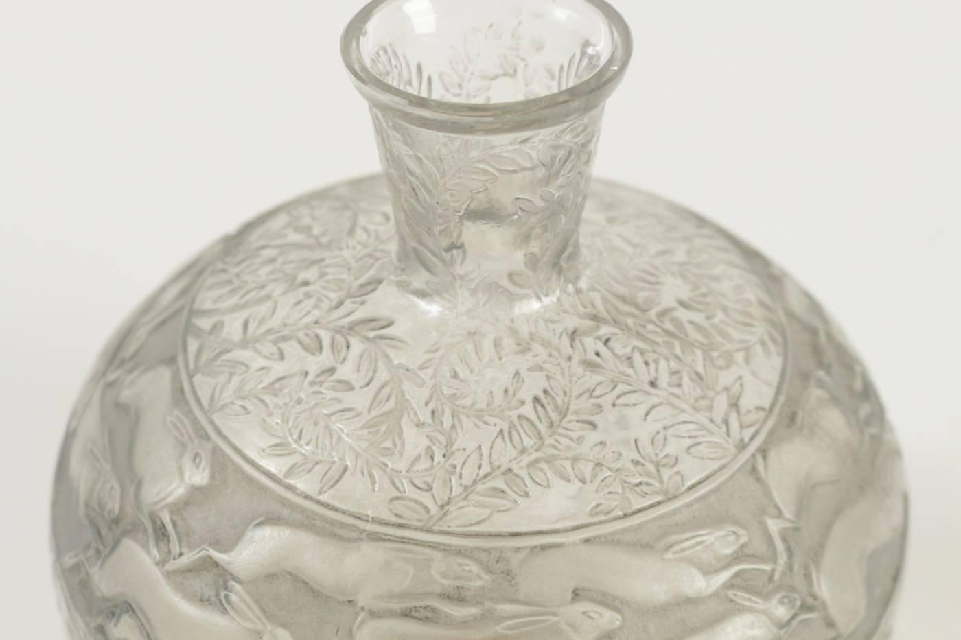 Tall bulbous grey patinated, clear and frosted glass container with a conical somewhat long neck and decorated with a band of running hares in between foliageBibliographie: Félix Marcilhac, “René Lalique, catalogue raisonné de l'oeuvre de verre,”