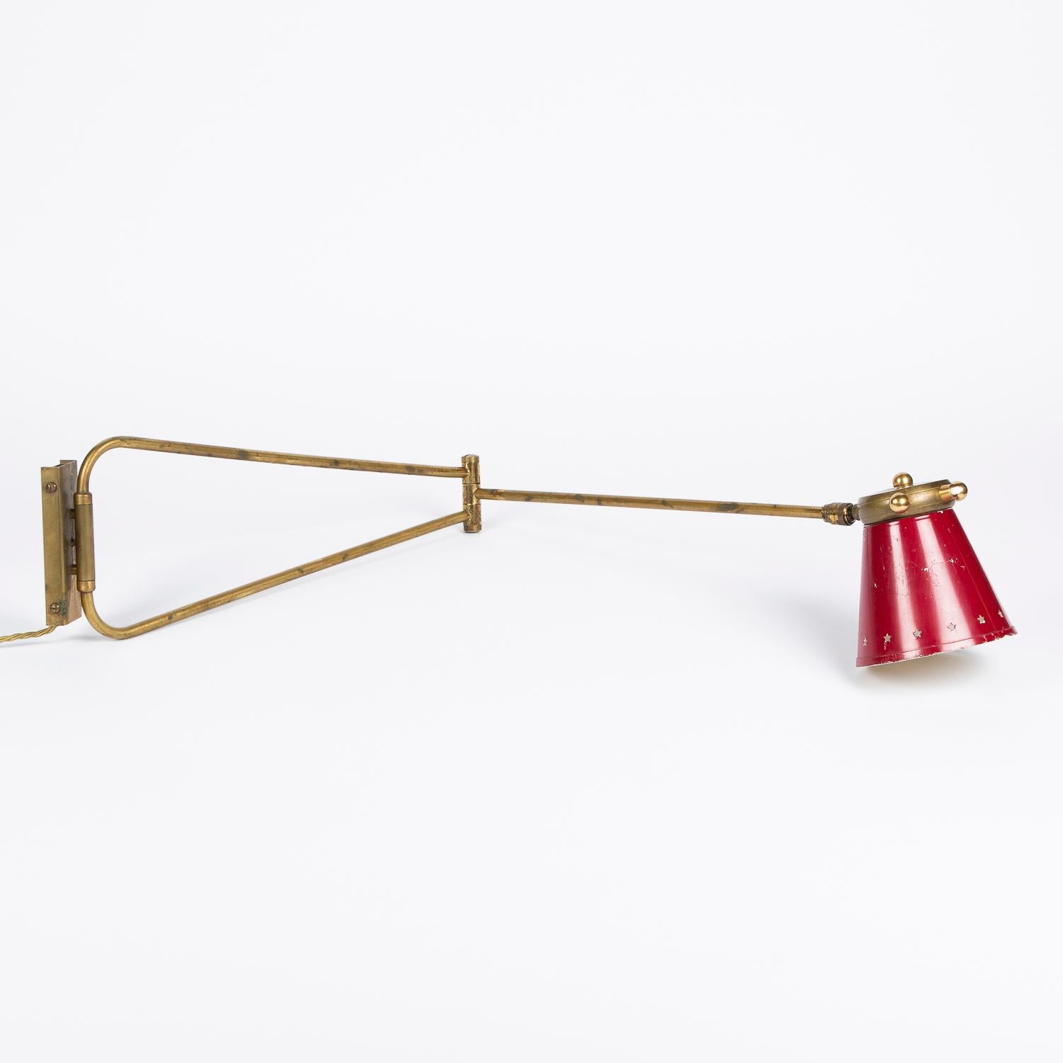 A 1950s double swing arm wall lamp designed by René Mathieu for Maison Lunel.

Crimson red shade, with white interior, pierced with stars. Brass articulating arm, hinge, back-plate and cap. Some losses to the crimson red paint work.

Projection