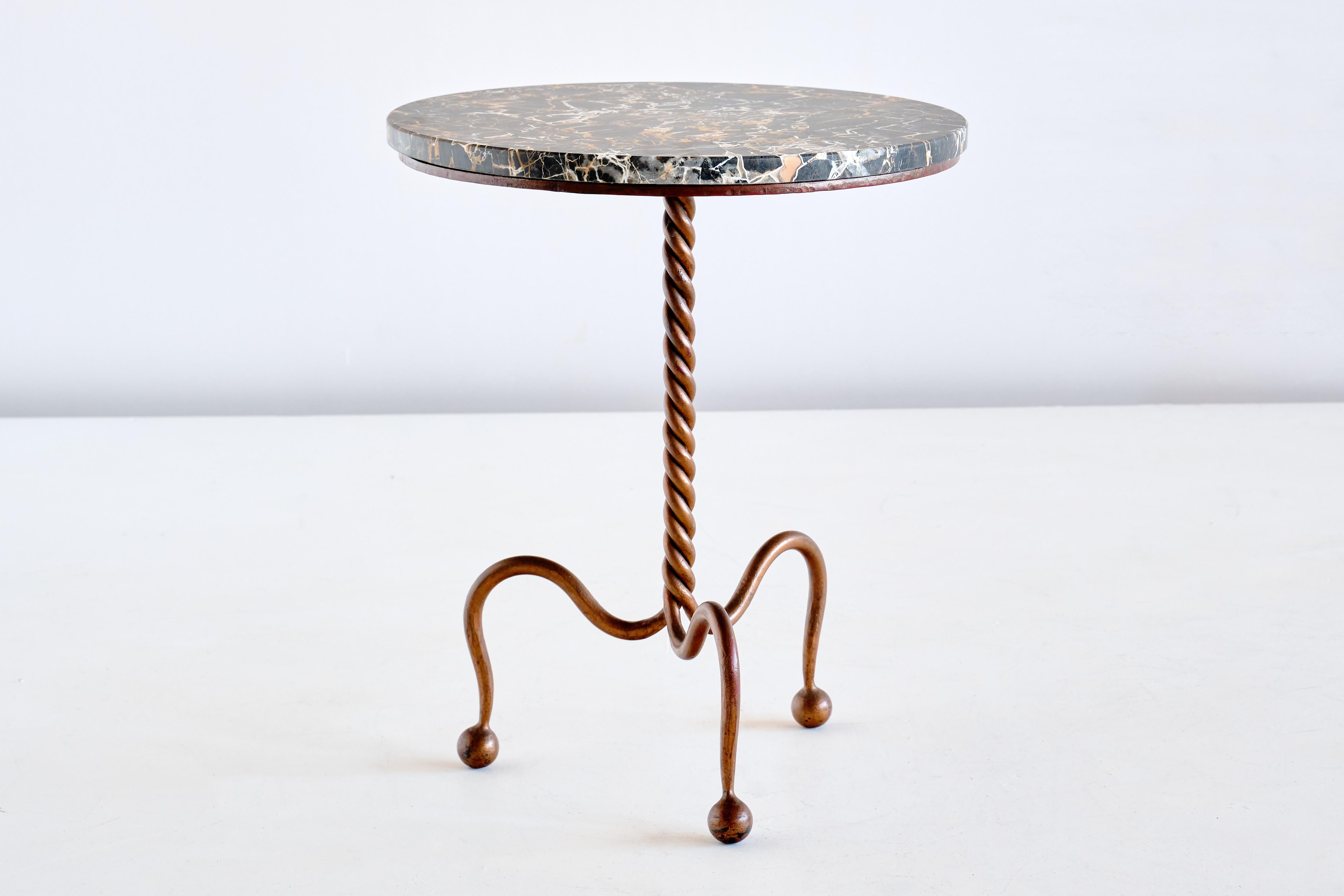This rare side table was produced in France in the late 1930s. The design is attributed to René Prou. The elegant gilded iron frame consists of three spherical legs attached to the curved legs leading to the interwined center base in a braided rope