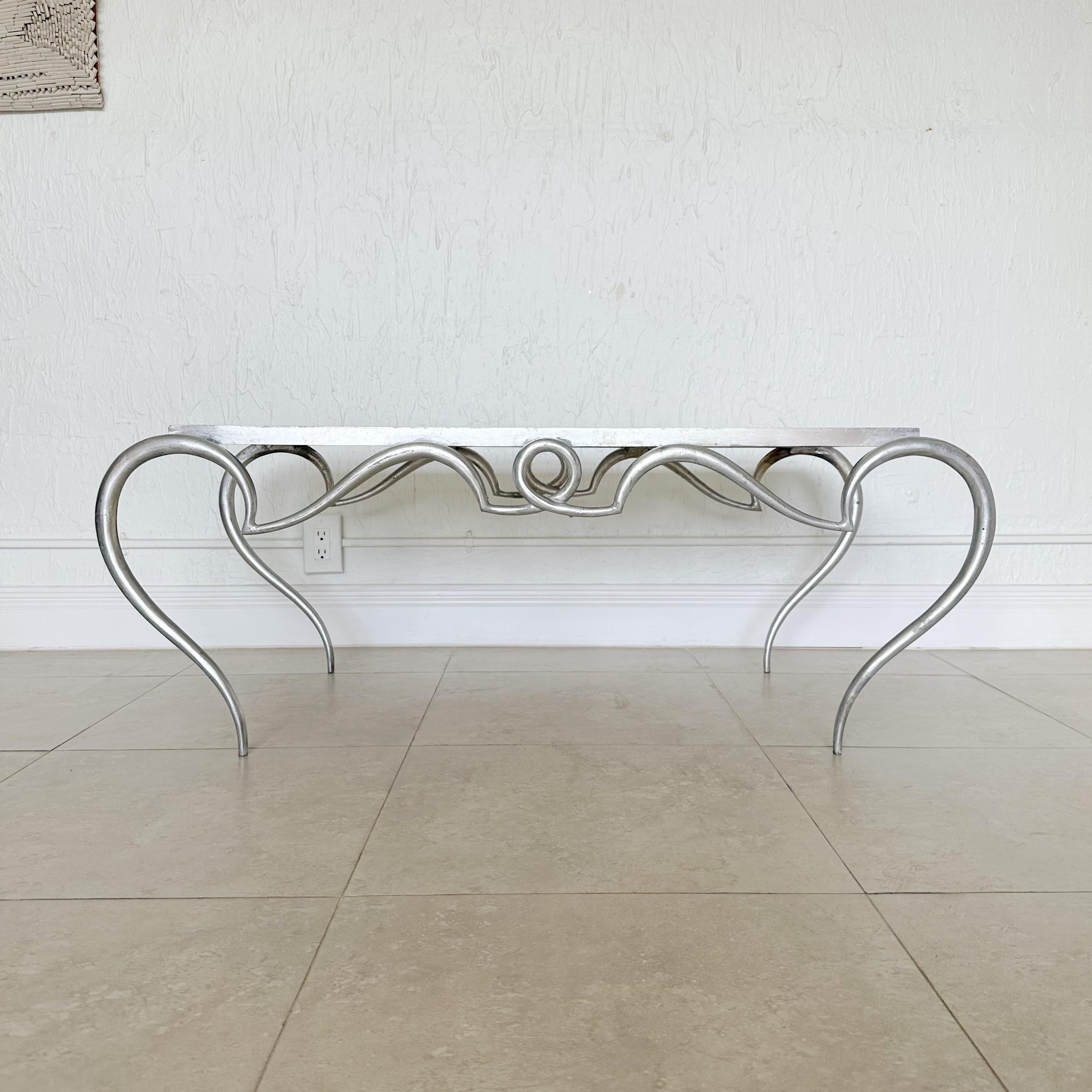 This coffee table is an interesting piece and
could be a good addition to any
home or collection. It has a unique
design, very ornate and intricate
scrollwork, as well as a replaced
beveled stone top. It features a
sophisticated silver leaf
