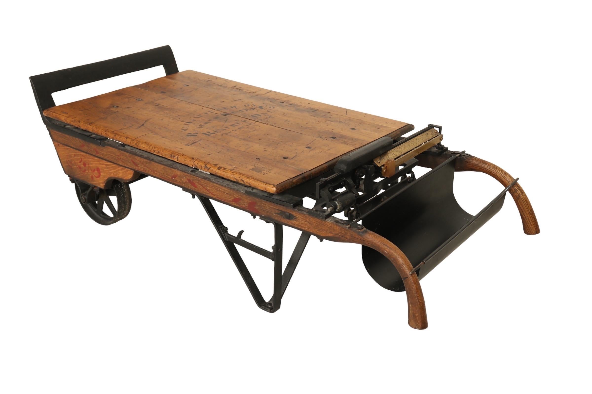An industrial dolly and grain scale coffee table patented in 1911 and manufactured by Renfrew Scale Co. of Ontario, Canada as stamped on the tabletop. The handles and beveled edge tabletop are made of oak. The weighing scale measure is brass and the