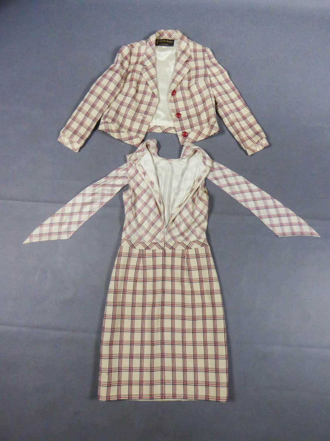 Circa 1970
France

Jacket and dress set in ivory nylon and woollen cloth with red and blue plaid from the 70s. Fitted jacked with wide-tabs on the hips closing on the front with front snap fasteners and three red leather buttons. Dress with straight