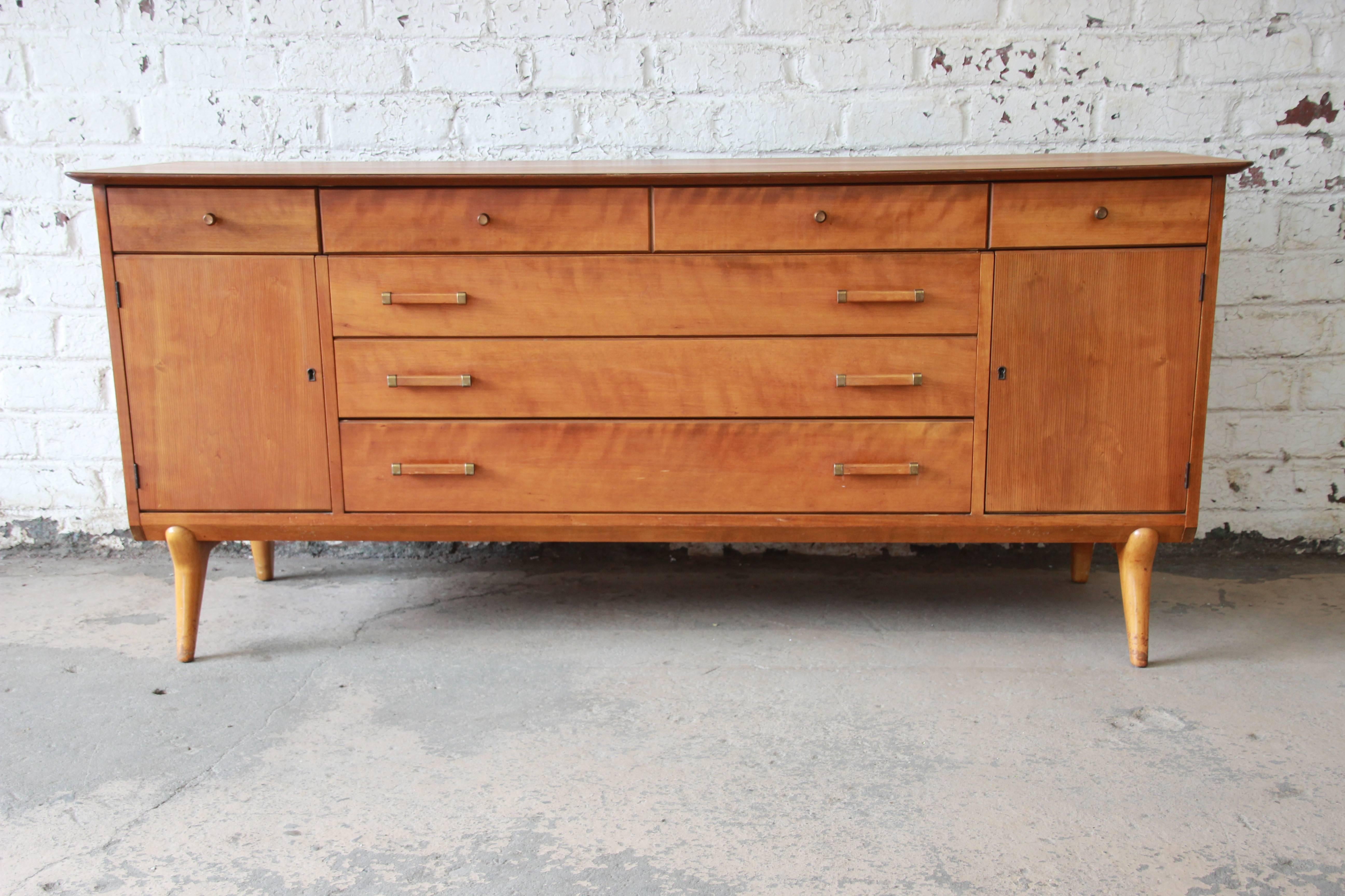 An outstanding Mid-Century Modern credenza or sideboard designed by Renzo Rutili for Johnson Furniture Co. The sideboard features gorgeous cheerywood grain and sleek midcentury design with tapered legs. It offers ample room for storage, with six