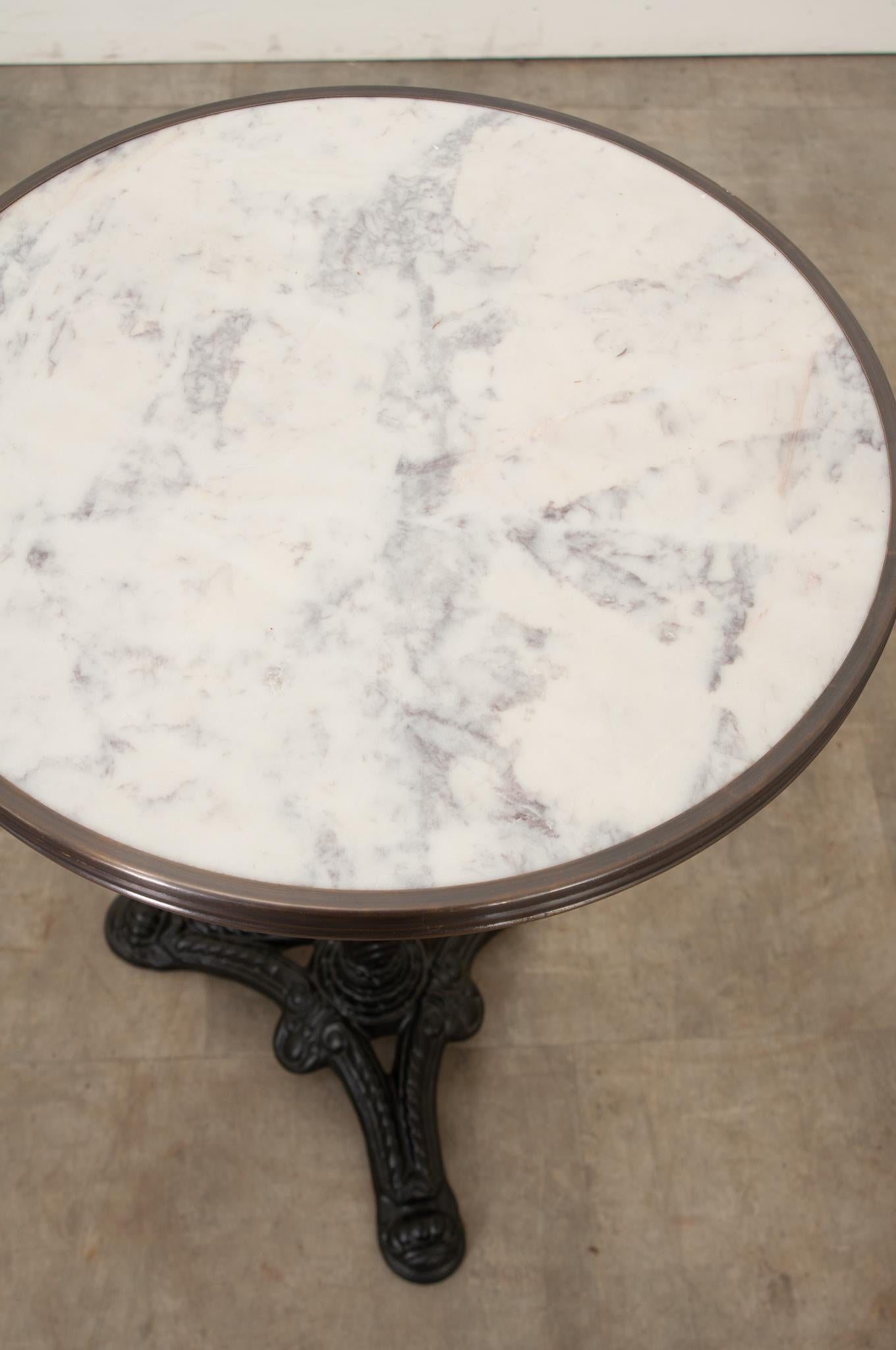 A classic Parisian style marble top & iron bistro table. A unique white marble top is banded by an antiqued brass trim. The base is a classic cast iron pedestal with three feet. This table can be disassembled for shipping or storage. If using this