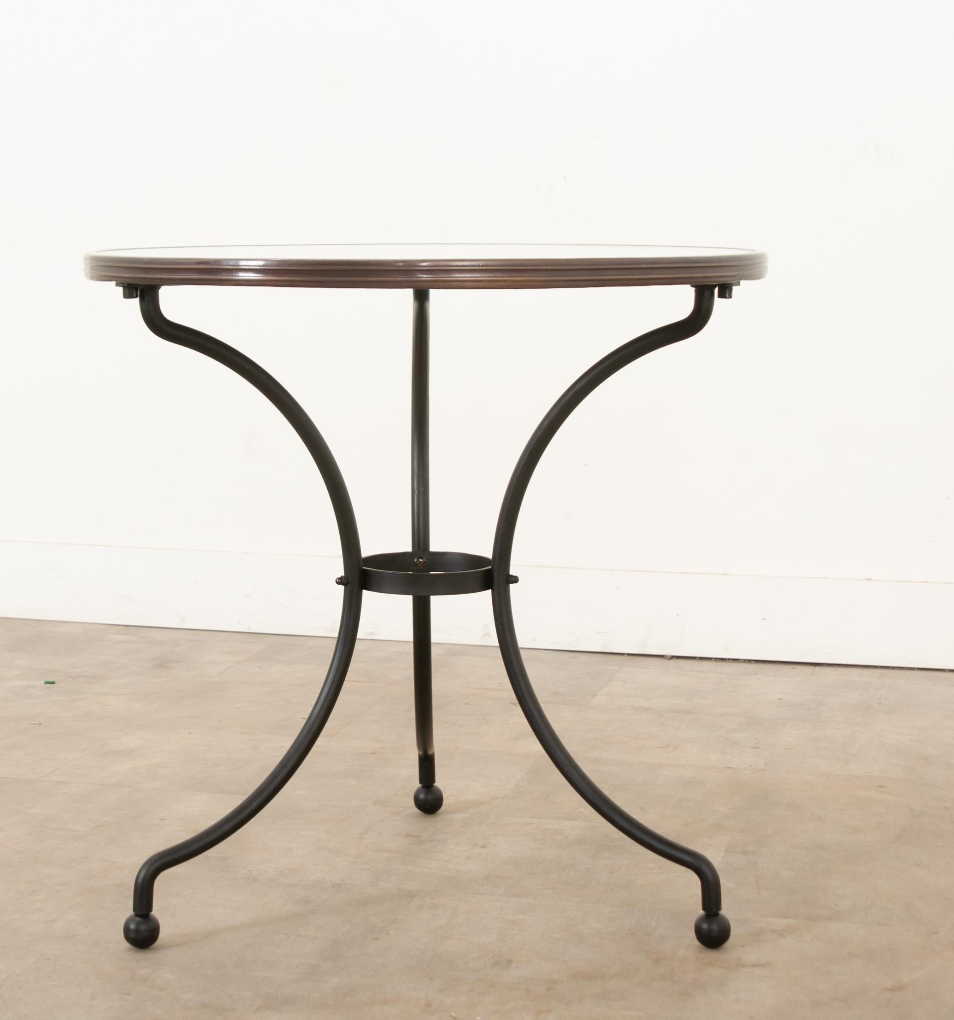 A classic Parisian style marble top & iron bistro table. A unique white marble top is banded by an antiqued brass trim. The base is classic in design, with 3 legs secured by a stretcher constructed out of cast iron. There are 3 steel prongs under