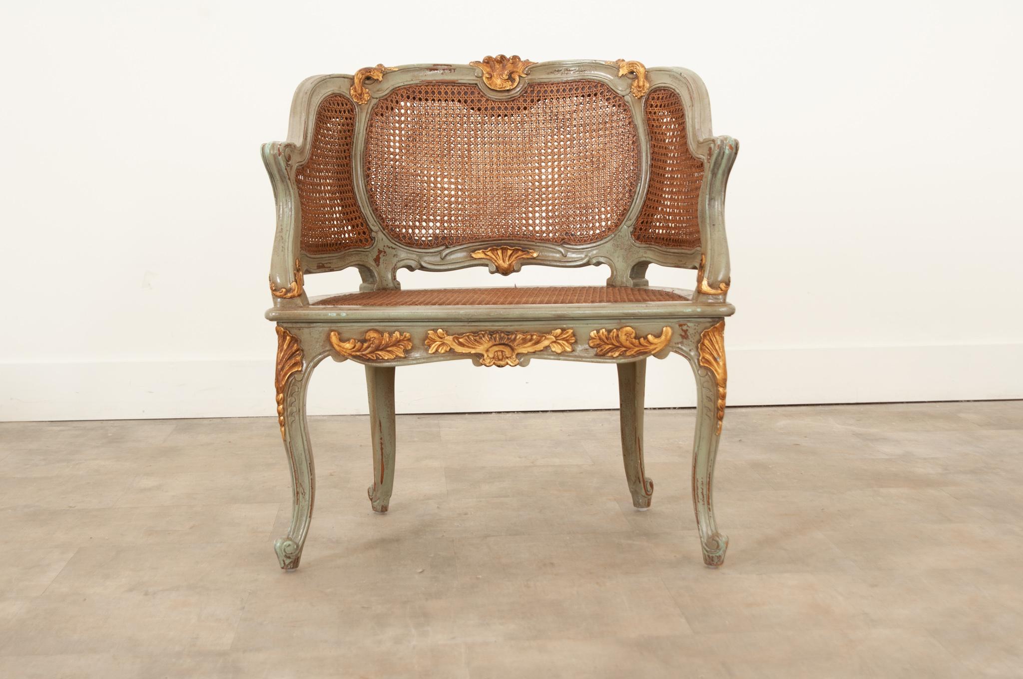 A fanciful reproduction Louis XVI style bergére featuring a wonderful trisected cane back and sides, surmounted by a foliate crest.  The cane seat and loose cushion sit about a carved frieze with a beautiful reserve of foliate pattern. The wood