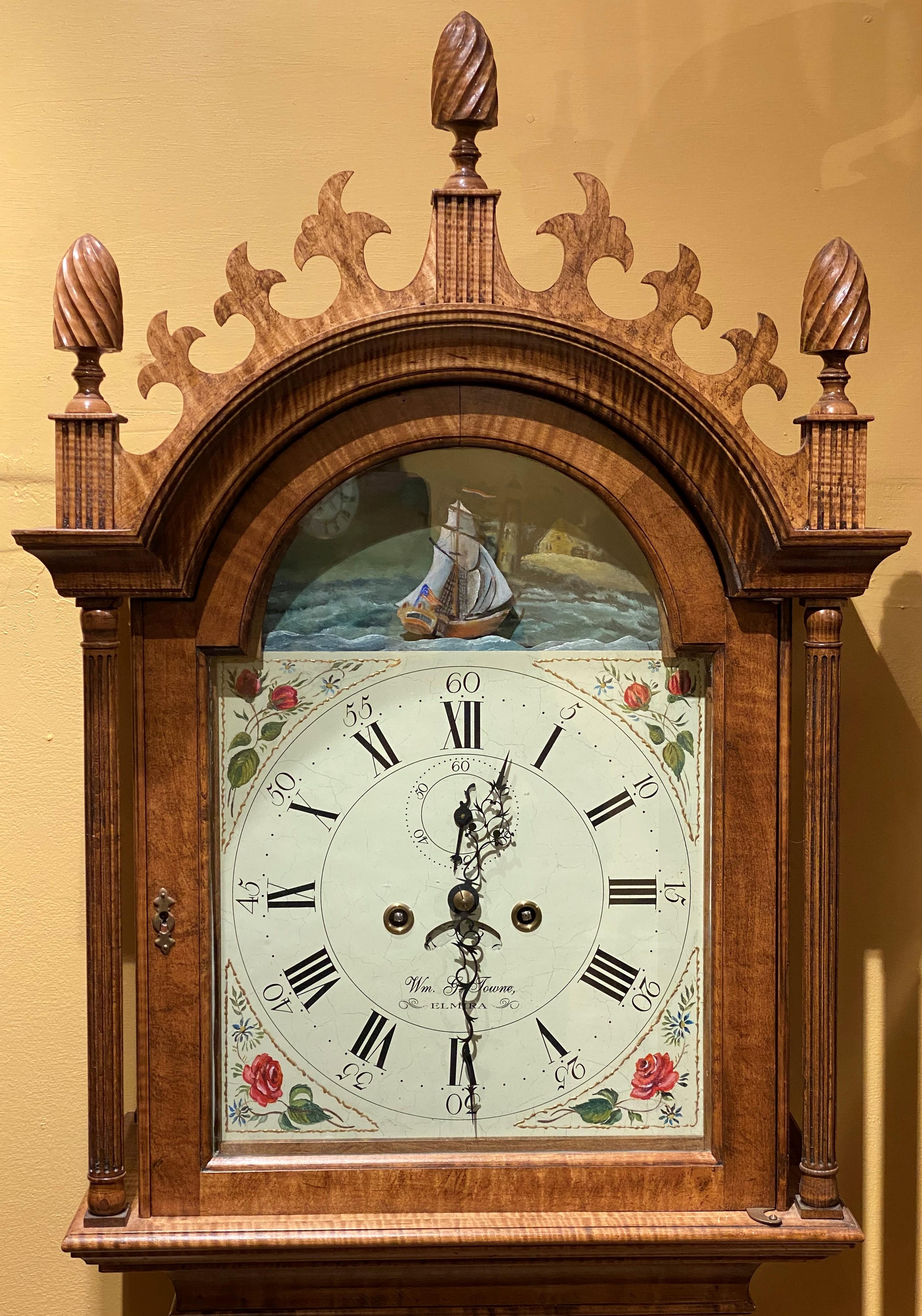 A New York reproduction of a Thomas Jackson, Connecticut 8-day time and strike tall case clock made by William G. Towne, Elmira. Weight driven movement in a tiger maple case with wave fretwork on the crest. The three carved flame finials are on