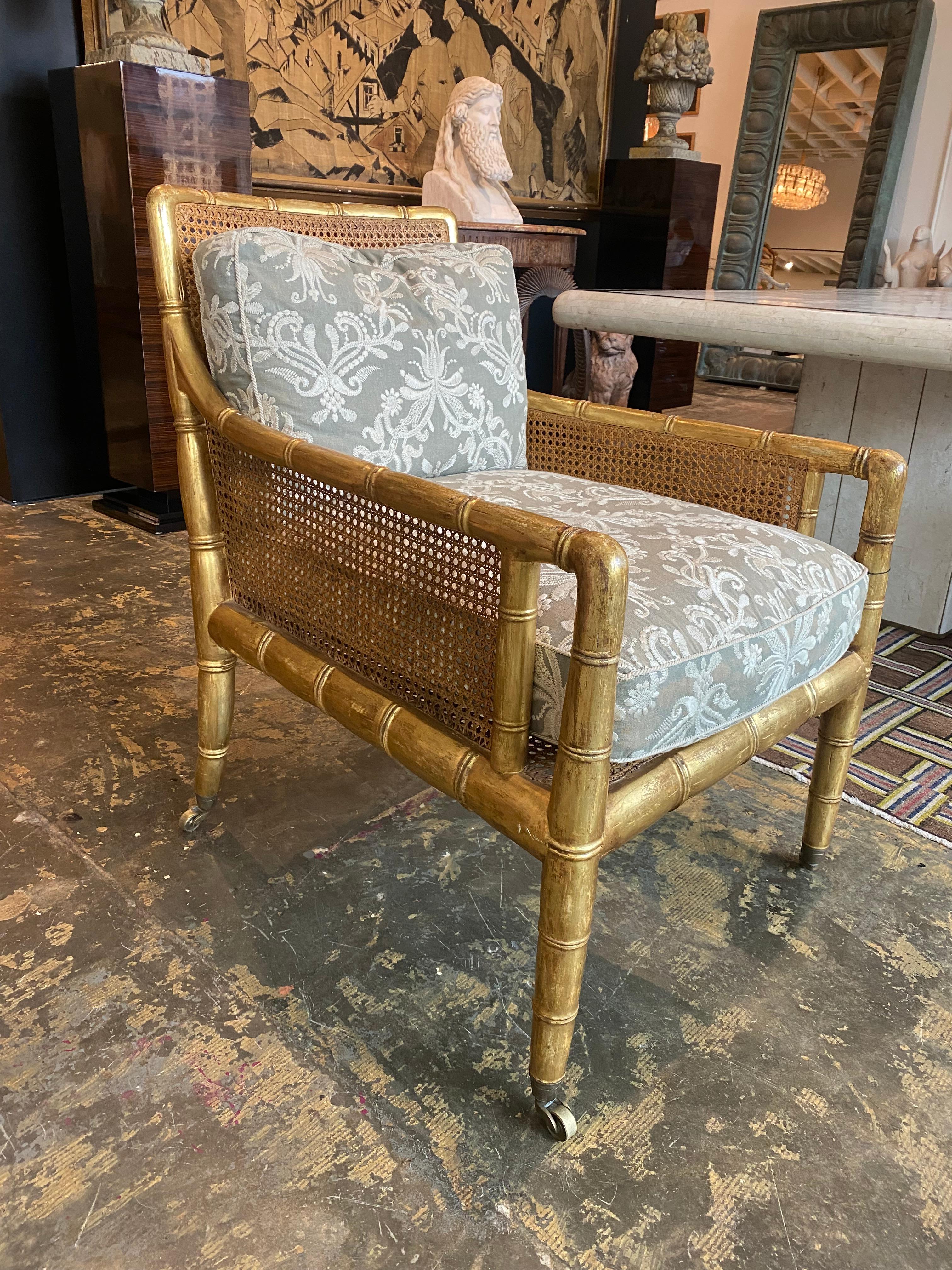 A beautiful reproduction Regency gilt bamboo caned bergere in excellent condition with loose seat and back cushions in an embroidered linen. Brass casters terminating the legs. The chair was manufactured by Dessin Fournir and was a sample in one of