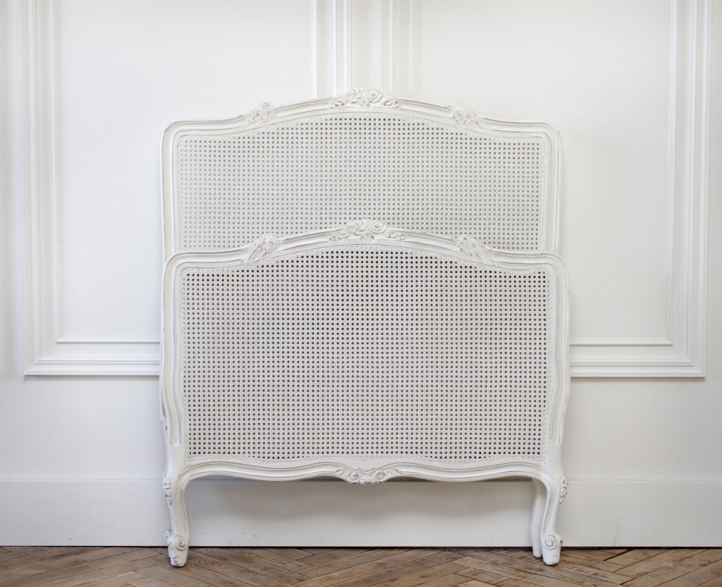 Reproduction twin carved and painted Louis XV style French bed with cane.
Painted white with subtle distressed edges, this bed has delicate carved flowers at the top, with a cane headboard and footboard. Cane is in good condition.
Measures: 43