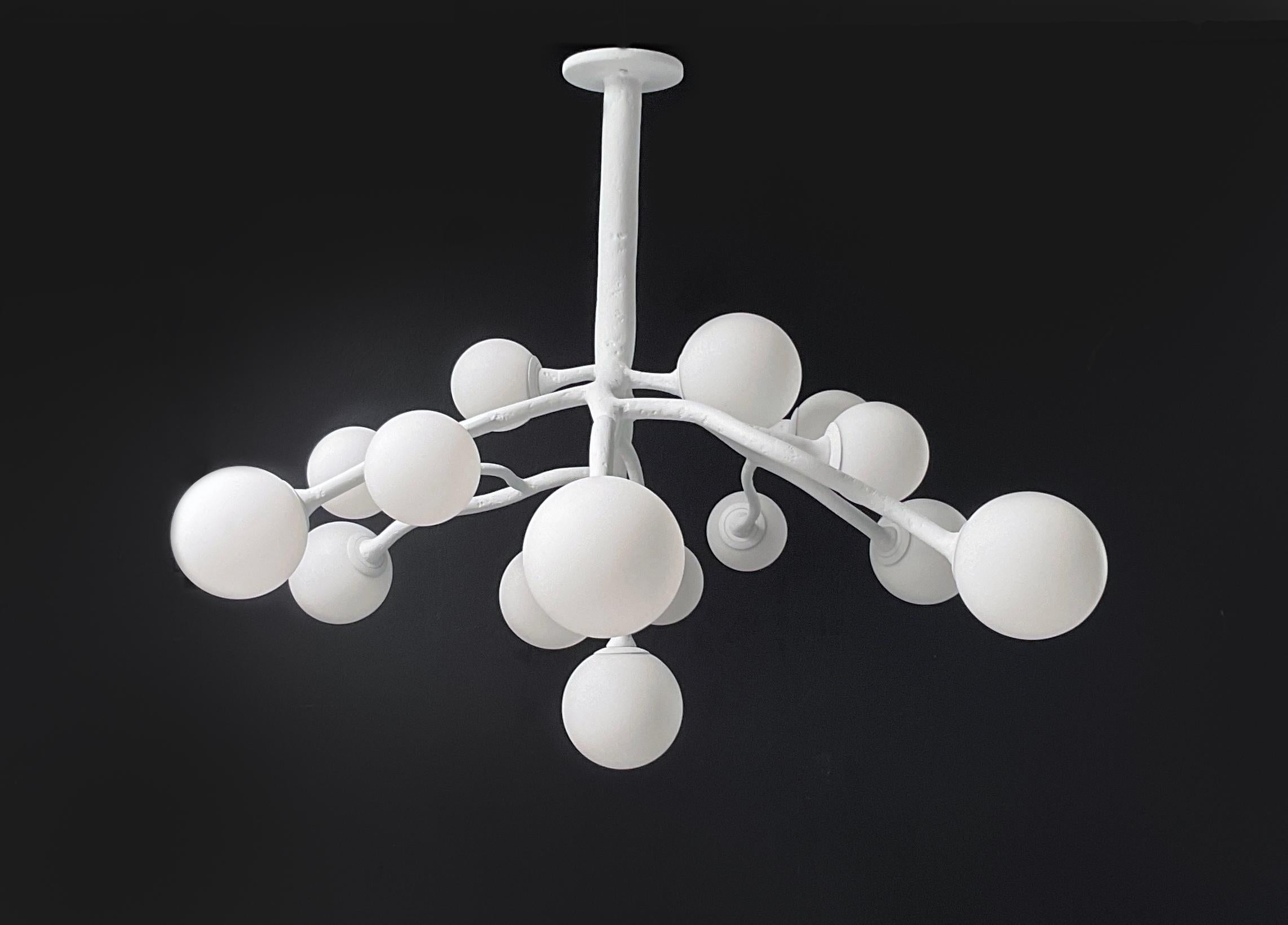 Il lampadario République di Bourgeois Boheme Atelier evoca la tensione poetica tra asimmetria organica e grazia architettonica. Composto da sedici globi di vetro opalino di diametro alternato di 5