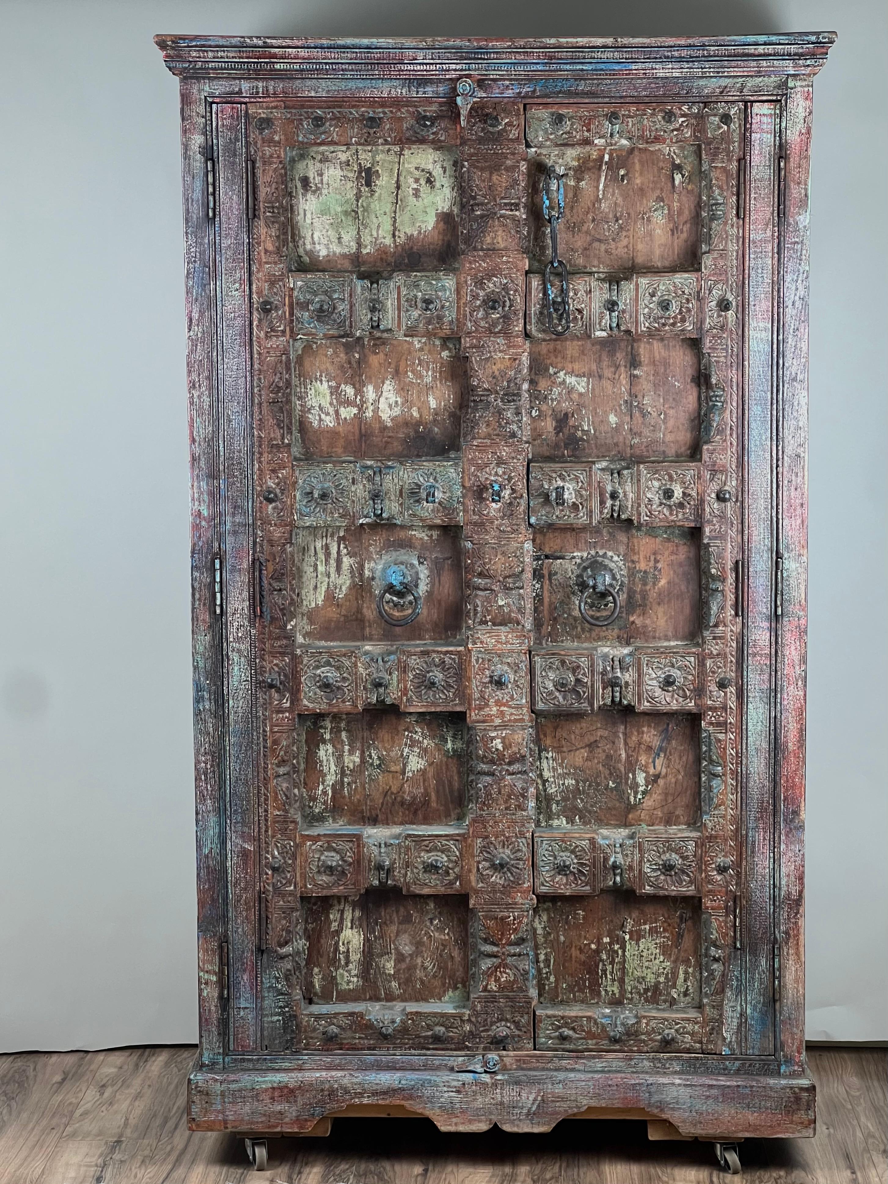 Cette armoire extraordinaire a été fabriquée à partir d'une porte indienne ancienne, réutilisée pour créer un meuble de rangement remarquable qui met en valeur le savoir-faire et la patine séculaires. Les panneaux sculptés et les ferronneries
