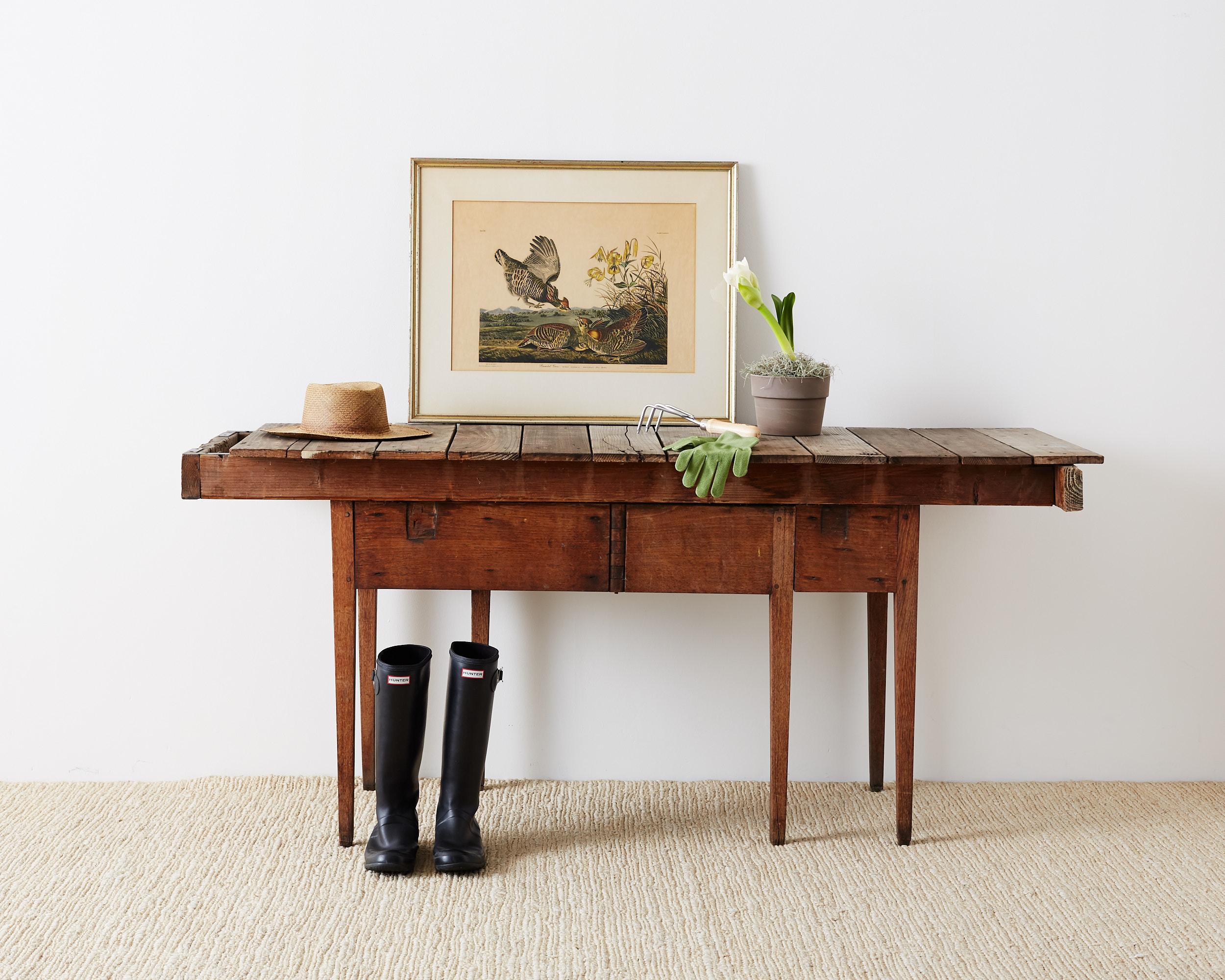 Repurposed Primitive style wooden gardening table or work table. Features an original drop leaf base made of mahogany still retaining its swing out gate legs on each side. Now having a large plank top work surface for gardening. Very distressed but