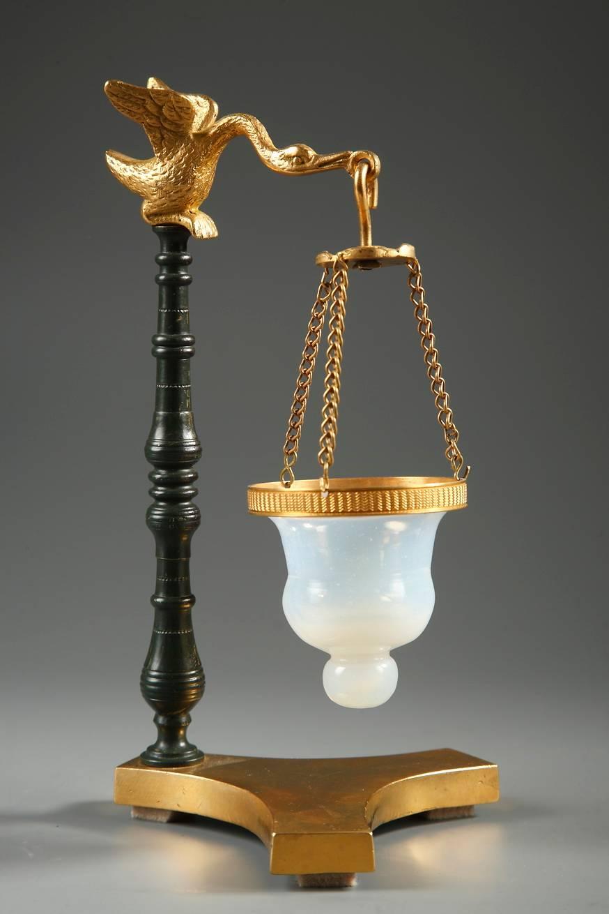 Charles X perfume burner (brûle-parfum) composed of a patinated bronze stem that rests on a triform plinth base. On the top of the stem a swan is spreading its wings and a small, white, opaline bowl is suspended from its beak. Three delicate chains