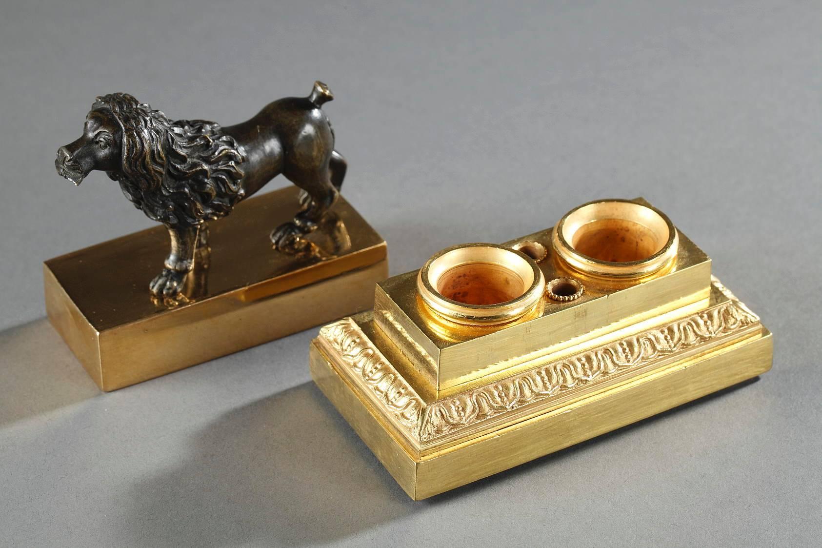 Restauration inkstand composed of a high, gilt bronze base with two inkwells and two penholders, decorated with a frieze of stylized flowers. The rectangular lid is topped by a patinated-bronze dog who is holding a letter in his mouth,
 
 circa