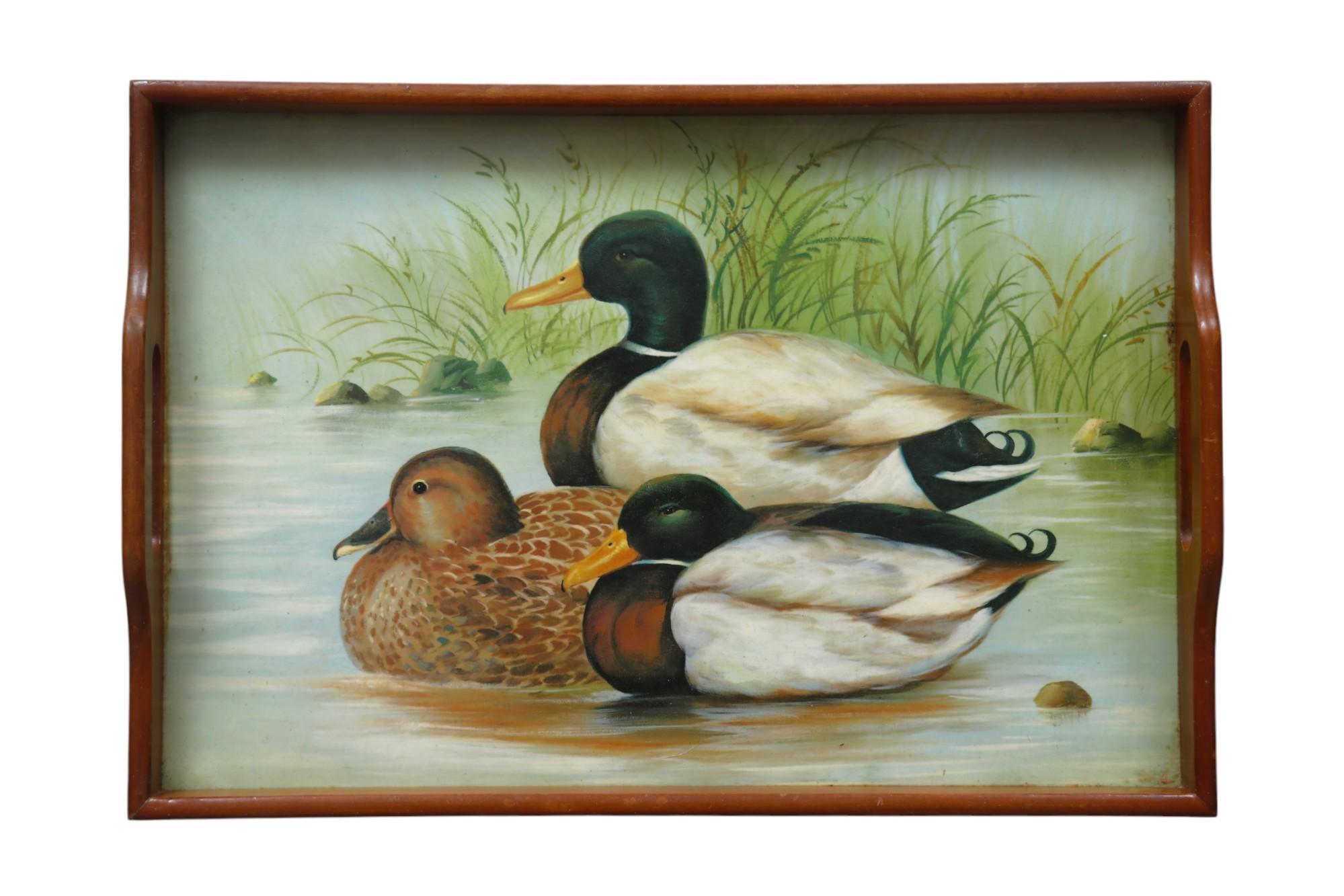 A painted wooden serving tray. The tray is painted with three mallard ducks, two males and a female resting by the water's edge. The wooden frame has a pierced handle at each side. 