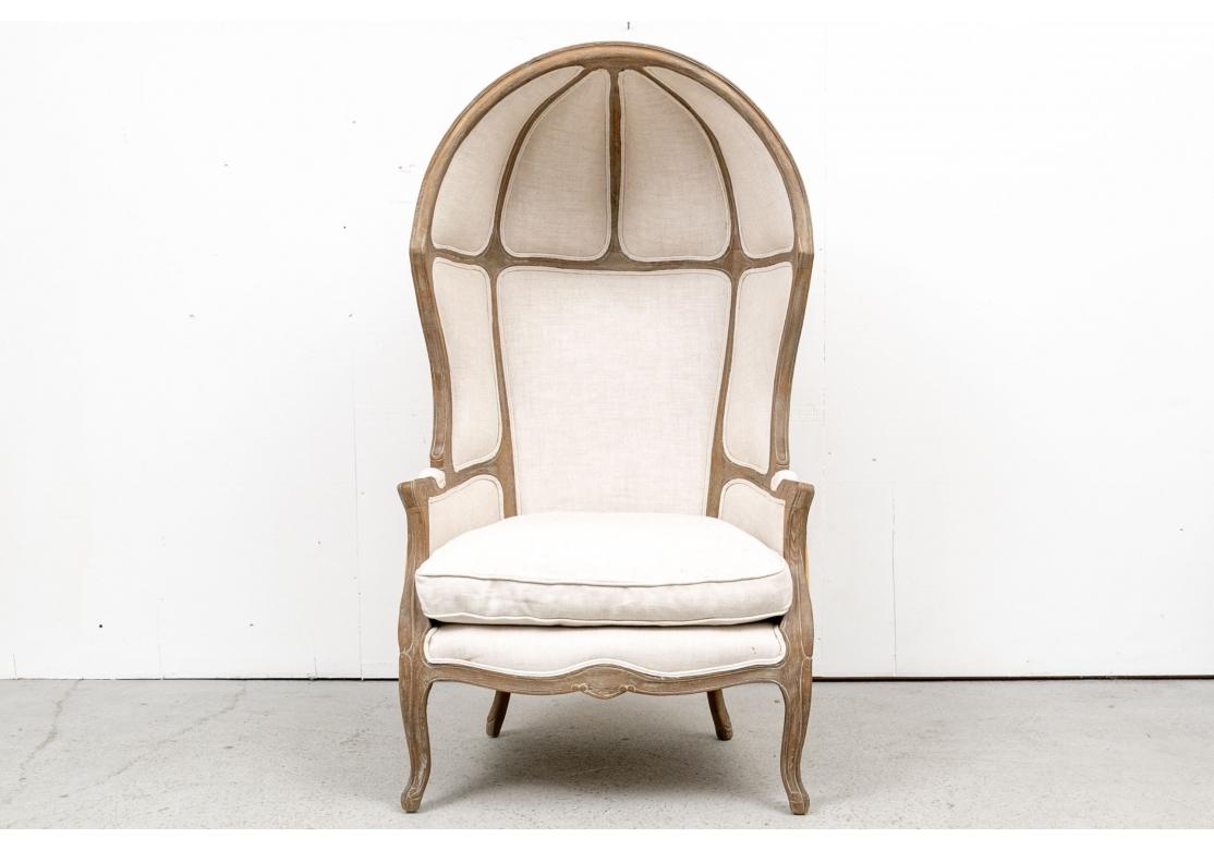 A beautiful hooded chair in the style of 18th c. chairs used by porters at the entrance to French chateaus. In natural wood burnt oak finish, with natural linen upholstery on the front and seat, and tan burlap on the back. With carved cabriole legs