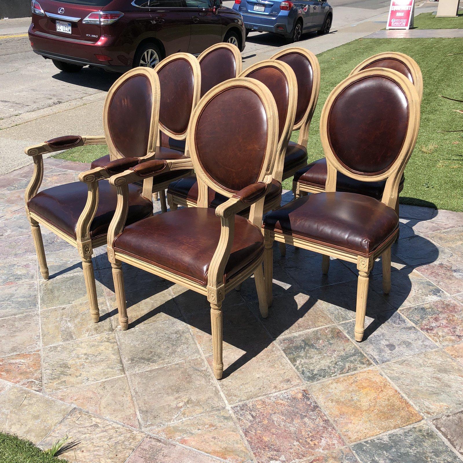 A set of eight vintage French round dining chairs by Restoration Hardware. This beautiful French-inspired set has hand-carved oak frames and hand-turned legs in a weathered oak drifted finish with rich brown distressed leather seats. Two armchairs,