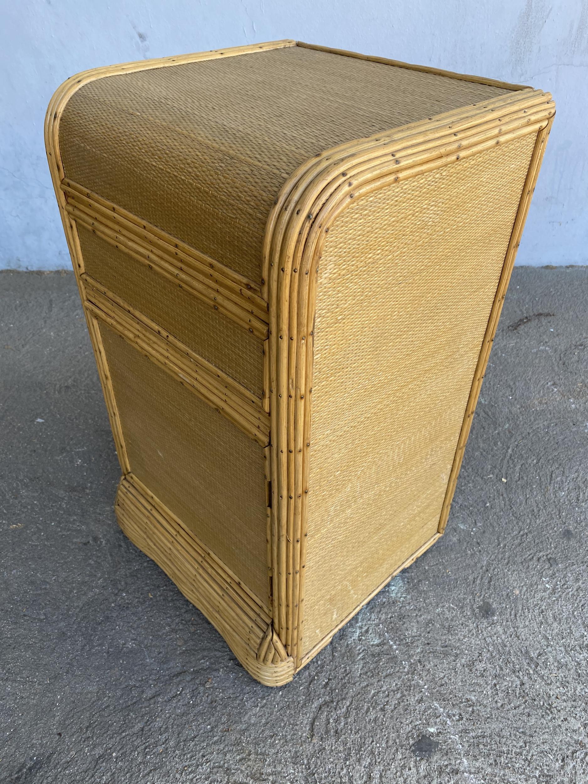 Streamline stick rattan side table with grass-mat coverings and edges are finished with brass nails. The side table features a single door that opens from the front.

Designed in the manner of Paul Frankl.

Restored to new for you.

All