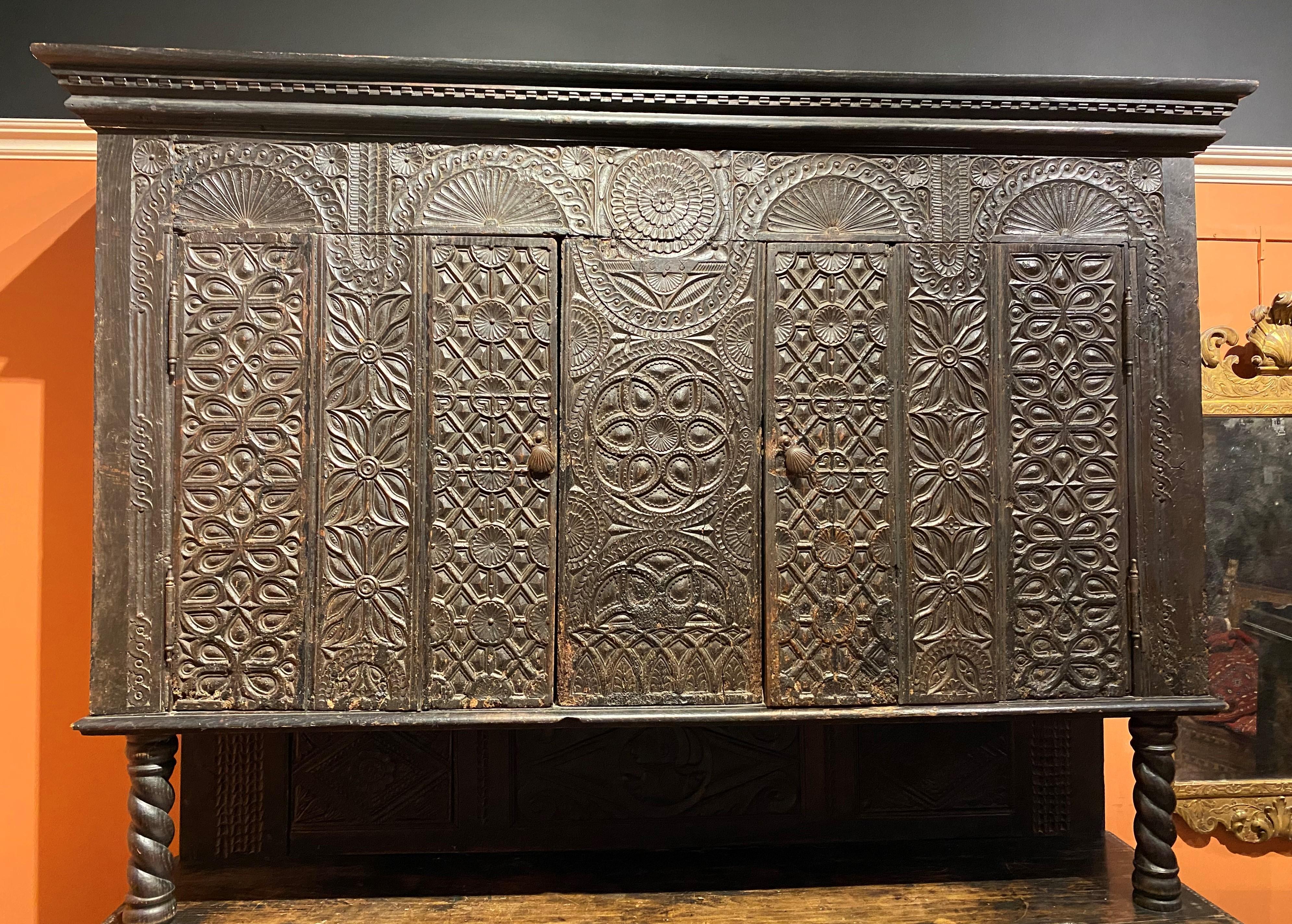 A splendid 17th century Continental two-part cupboard, its upper case with molded cornice with dentil molding, two carved doors opening to single interior shelves on each side, the fronts carved with geometric and arched relief designs, over a