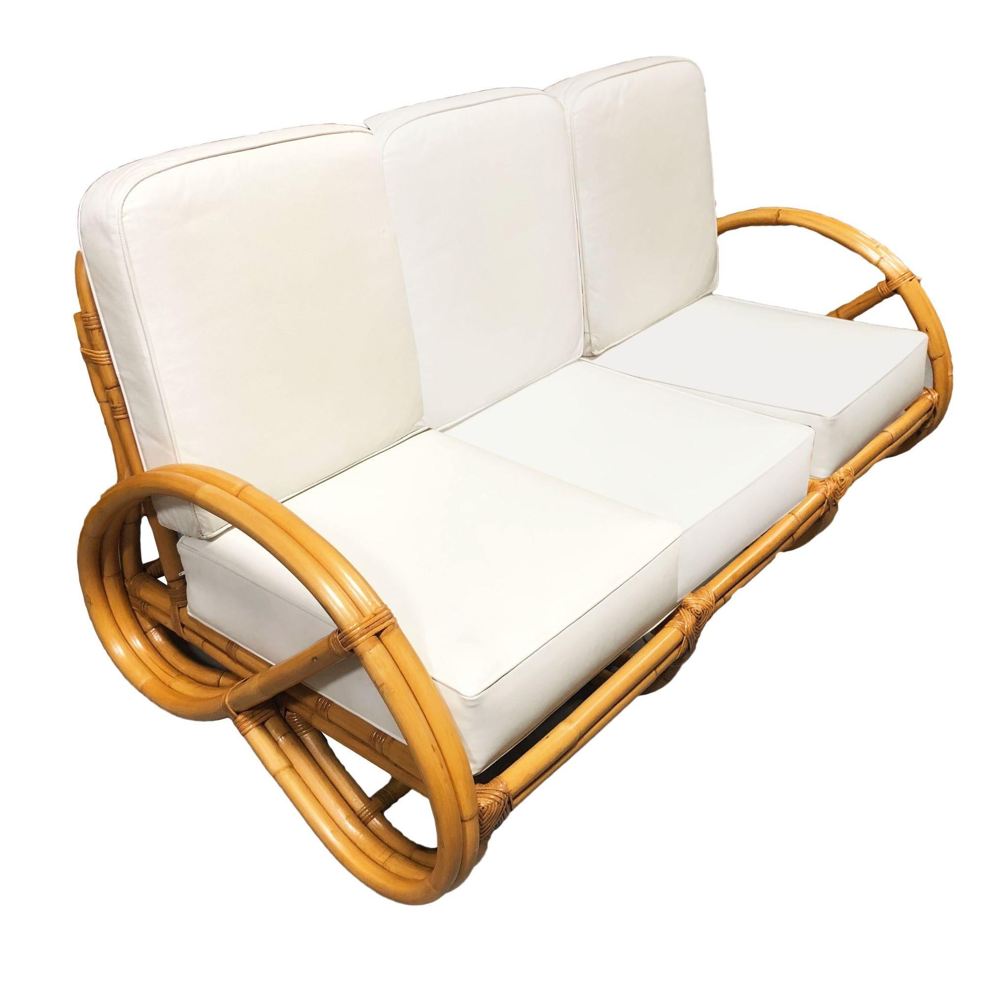 Questo divano in rattan a 3 posti con braccio pretzel 3/4 e poltrona abbinata, splendidamente restaurato e ispirato a Paul Frankl, è caratterizzato dal noto bracciolo pretzel 3/4 inverso su ciascuna estremità con un arco decorativo lungo la base.