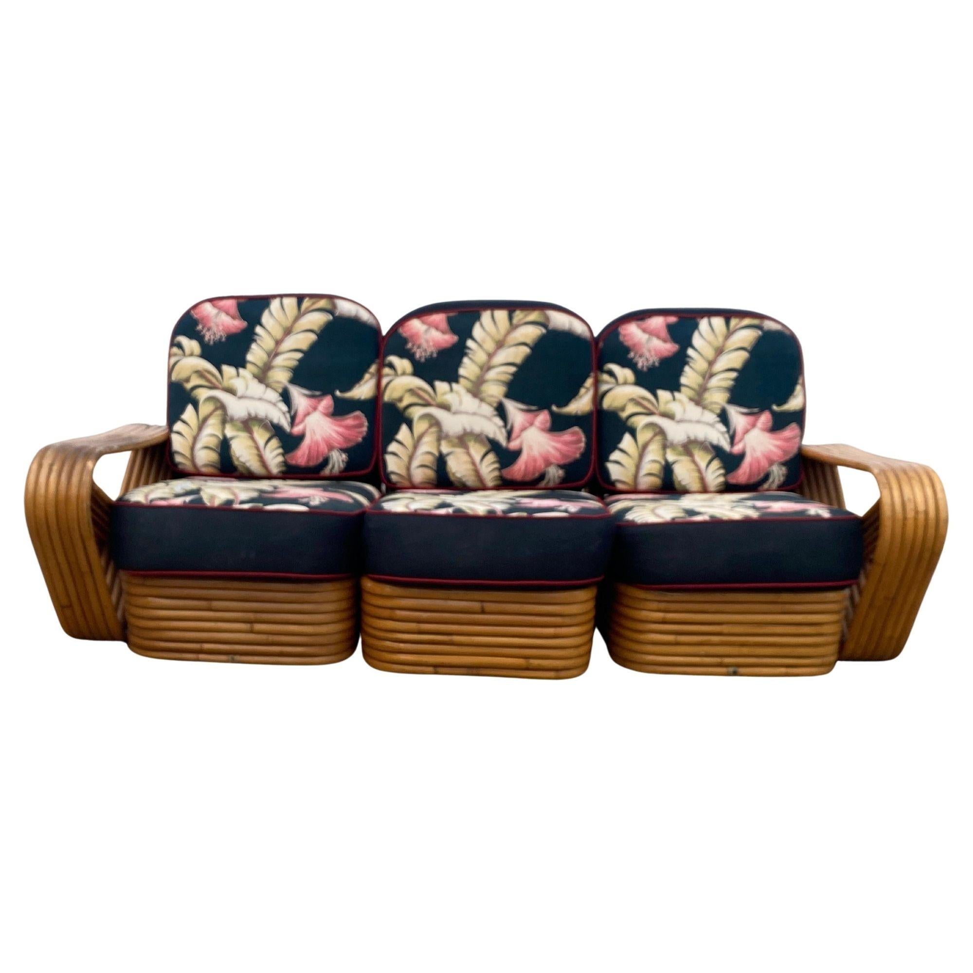 Paul Frankl-style rattan living room set includes a matching three-seat sectional sofa and a pair of lounge chairs. Both feature the famous six-strand square pretzel side arms and stacked rattan base originally designed by Paul Frankl. The seats are