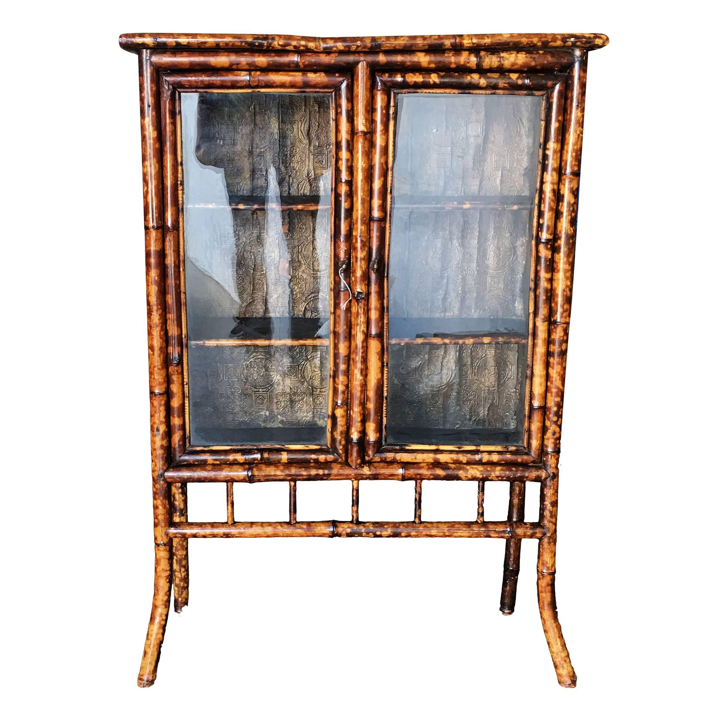 Antique three-tier shelf tiger bamboo breakfront cabinet with decorative hand-forged metal sides and two glass front doors resting on sculpted legs. 

Restored to new for you.

All rattan, bamboo and wicker furniture has been painstakingly